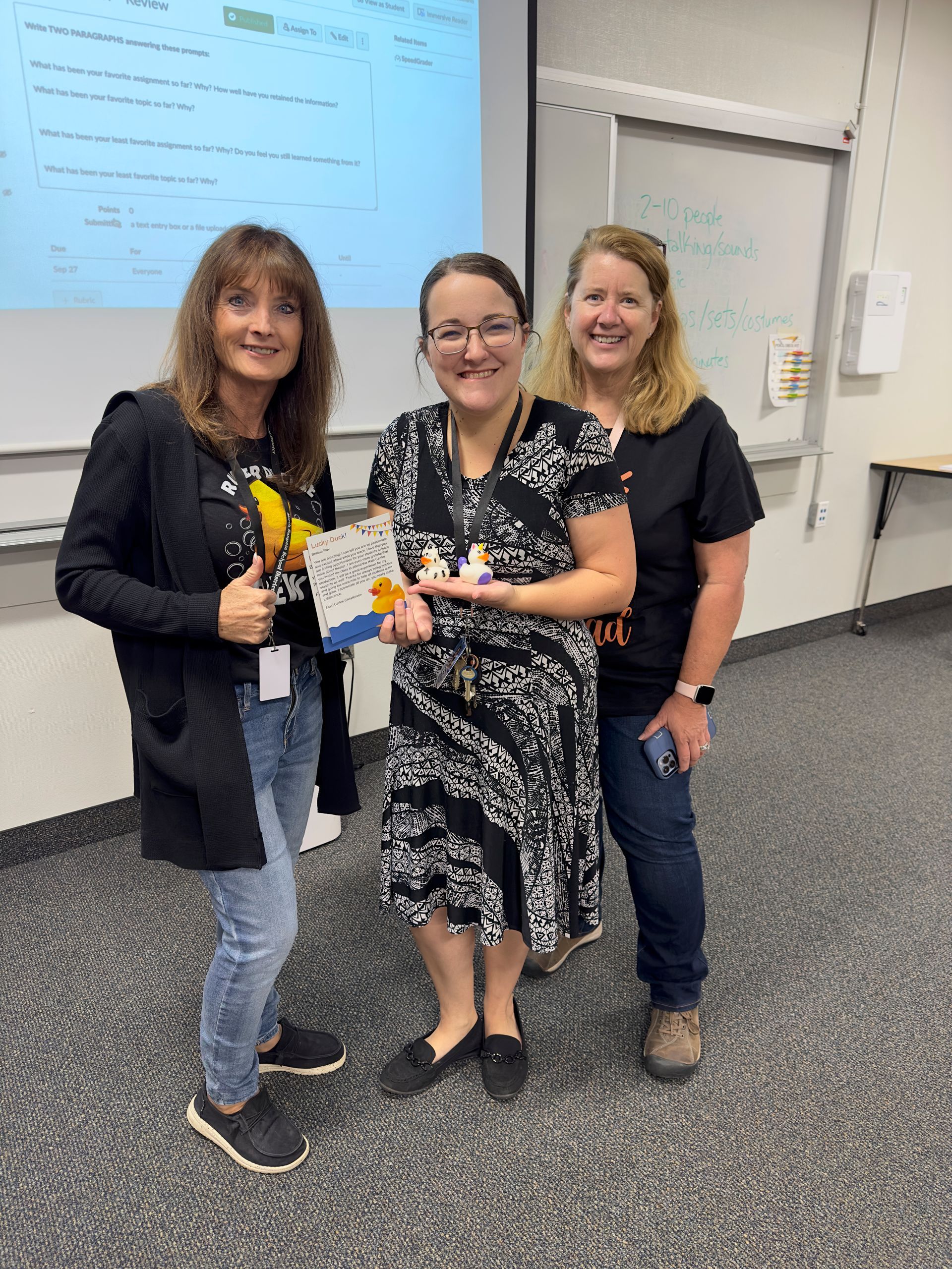 Three women are standing next to each other in a classroom.