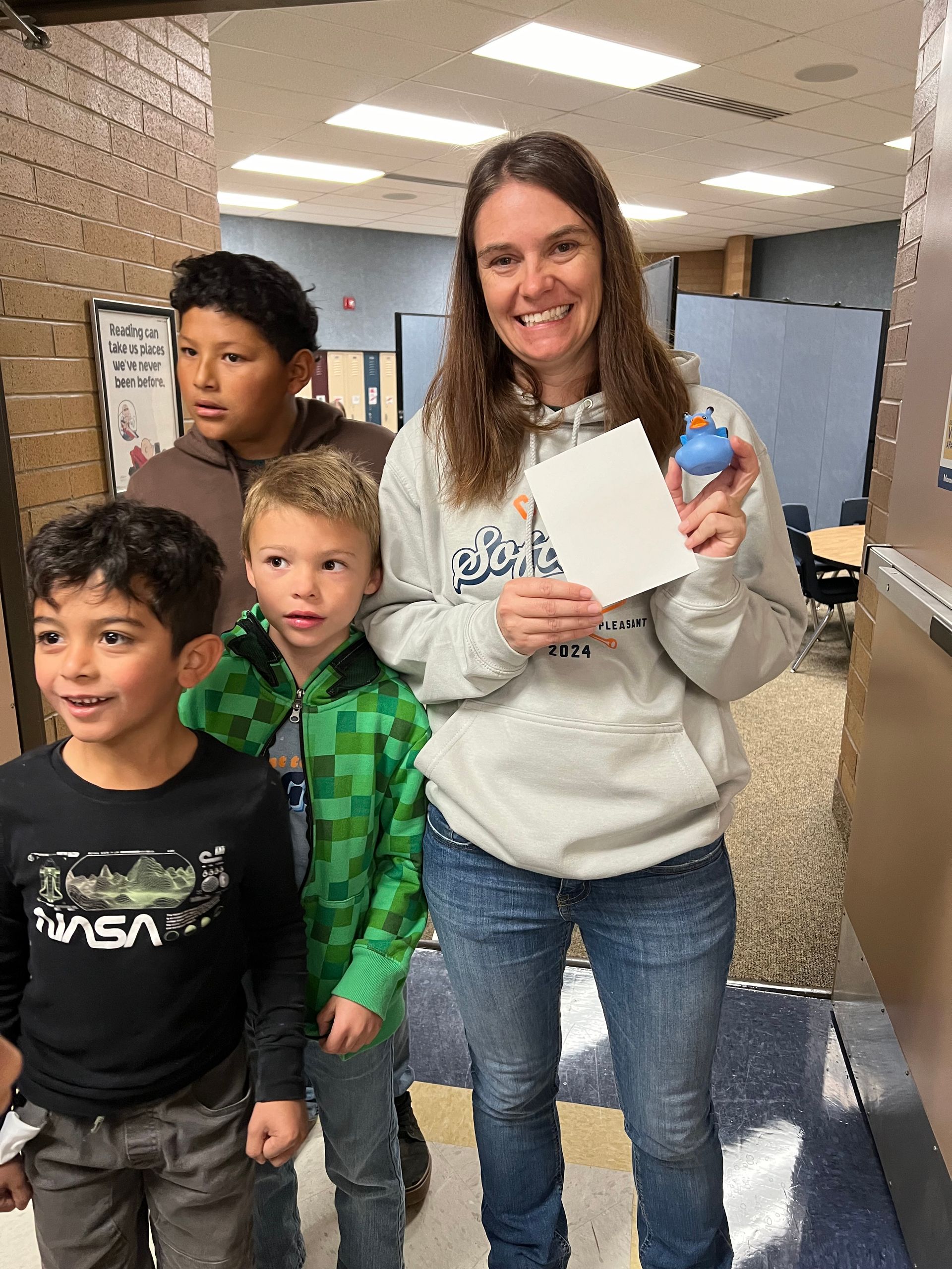 A woman is standing next to a group of children in a hallway.