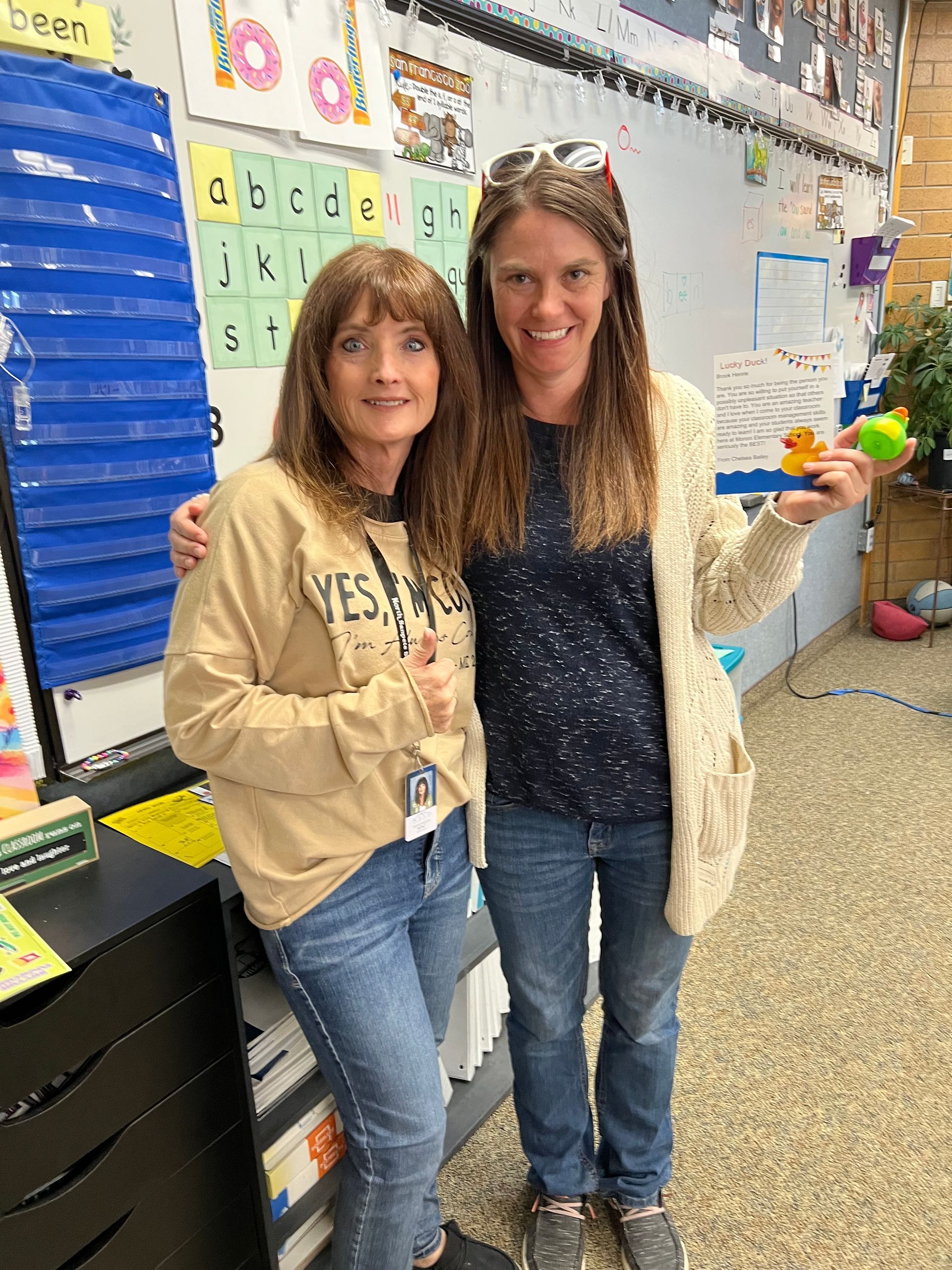 Two women are posing for a picture in a classroom.