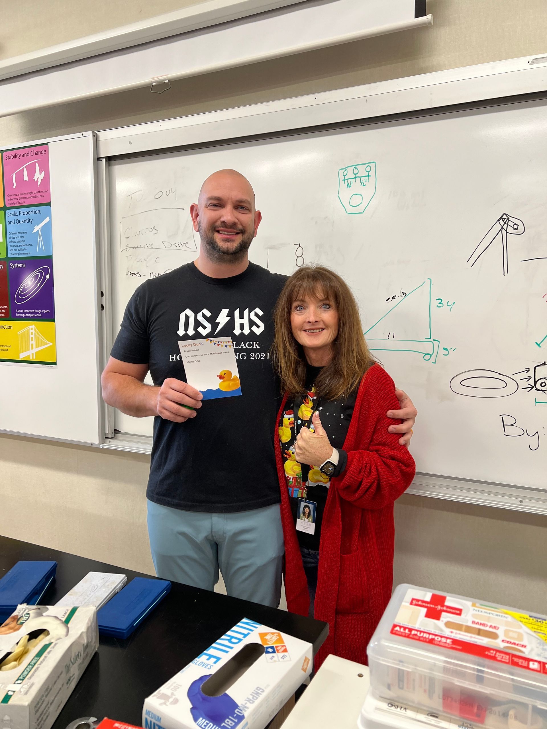 A man and a woman are standing in front of a whiteboard in a classroom.