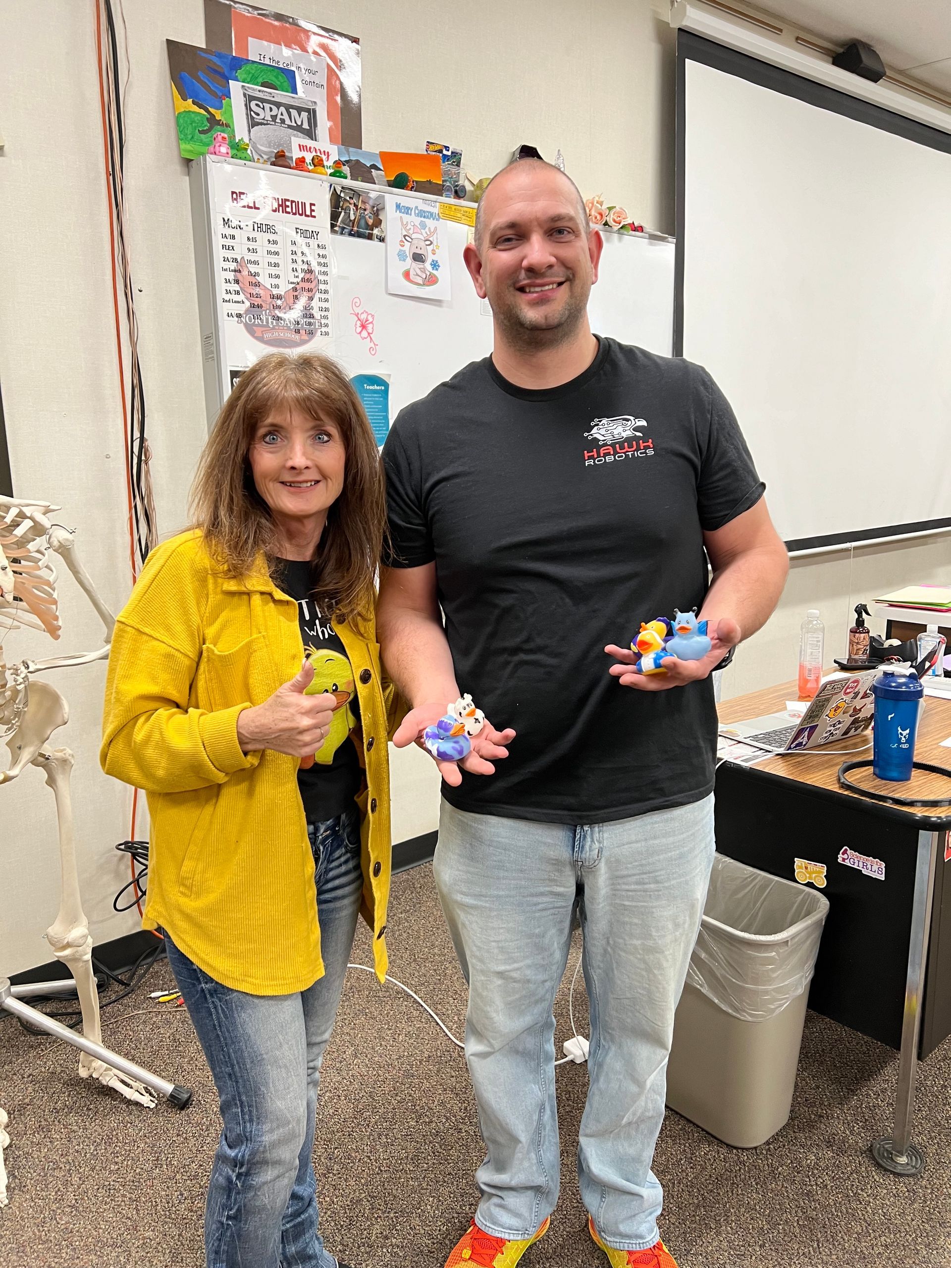 A man and a woman are standing next to each other in a classroom holding toys.