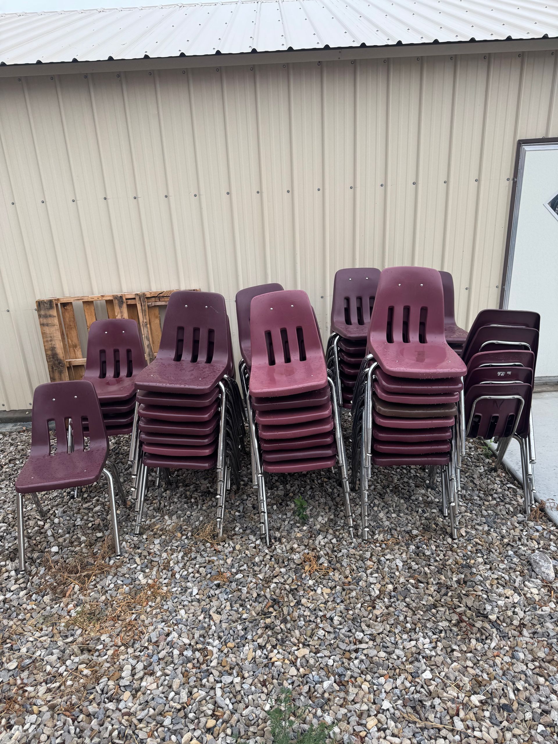 Stack of maroon school chairs outside a building.