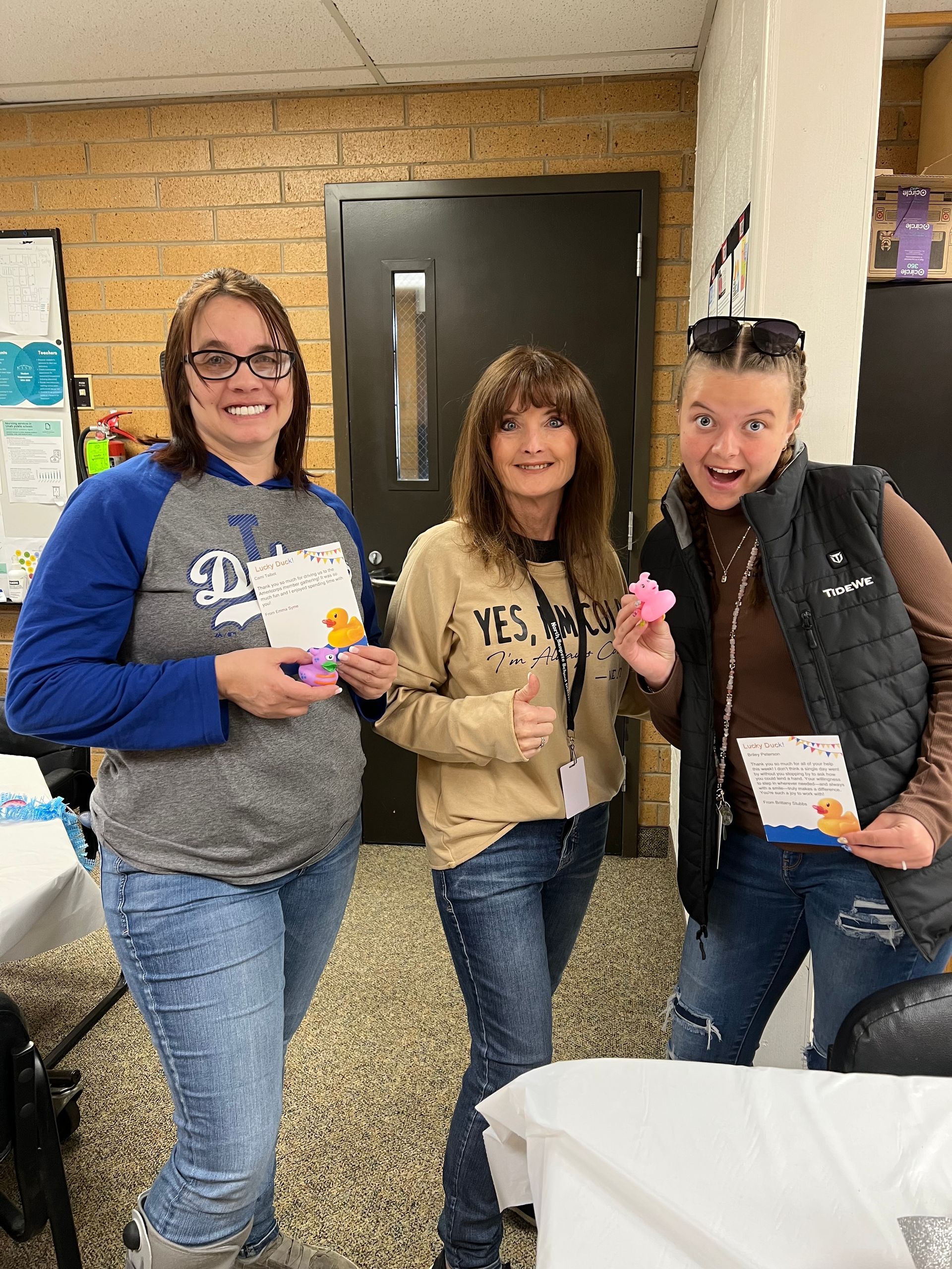 Three women are standing next to each other in a room holding donuts.