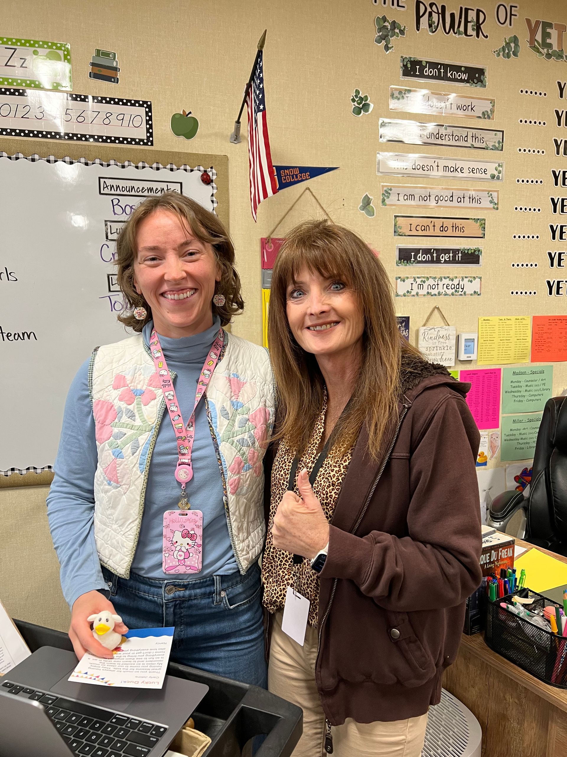 Two women are posing for a picture in a classroom.