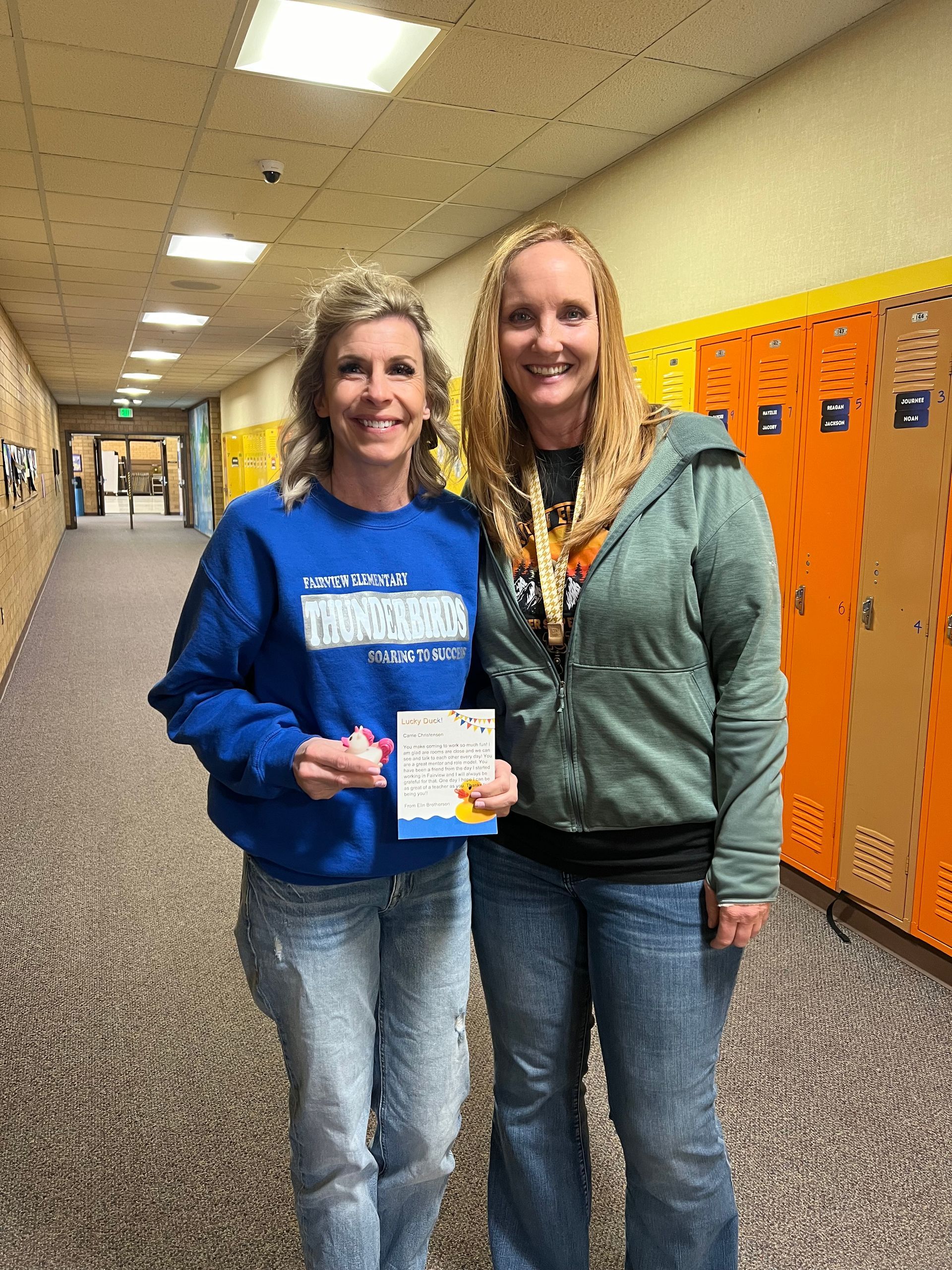 Two women are standing next to each other in a hallway holding a certificate.