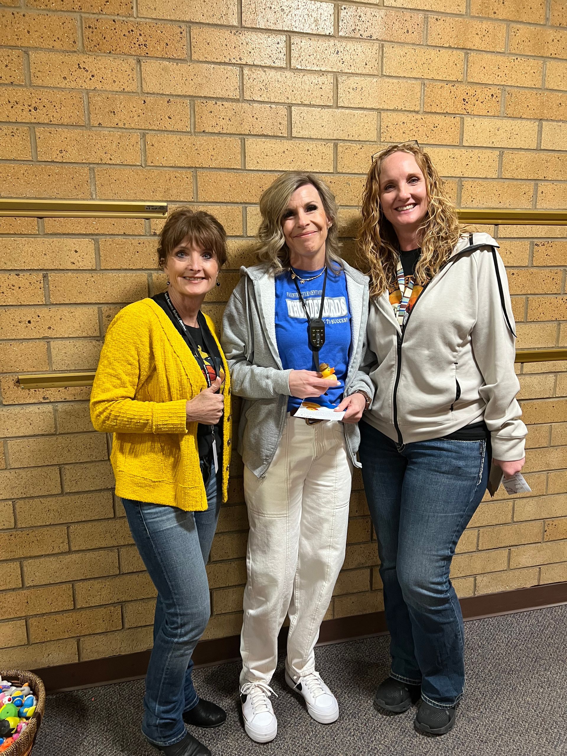 Three women are standing next to each other in front of a brick wall.