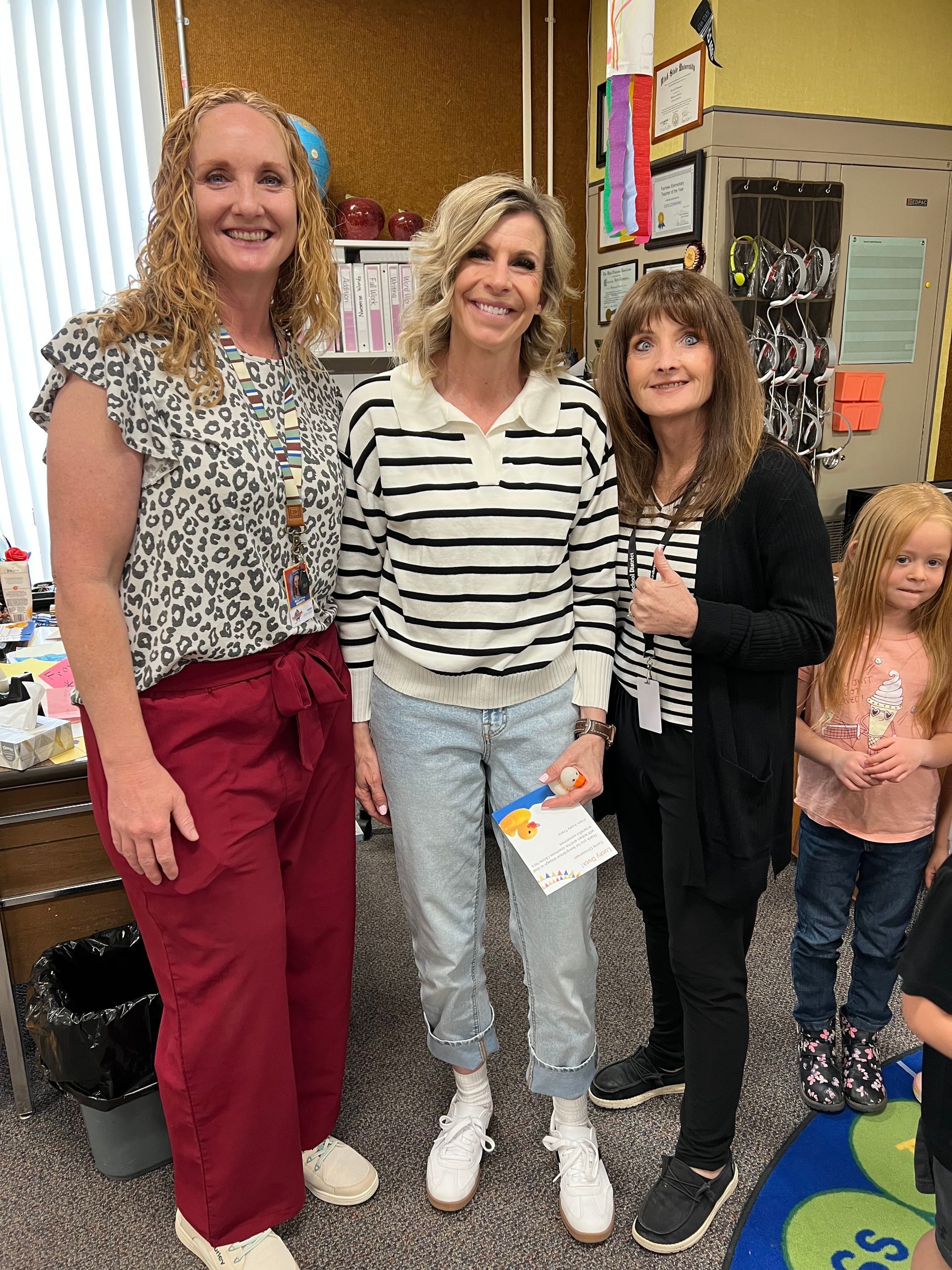 Three women are standing next to each other in a classroom.