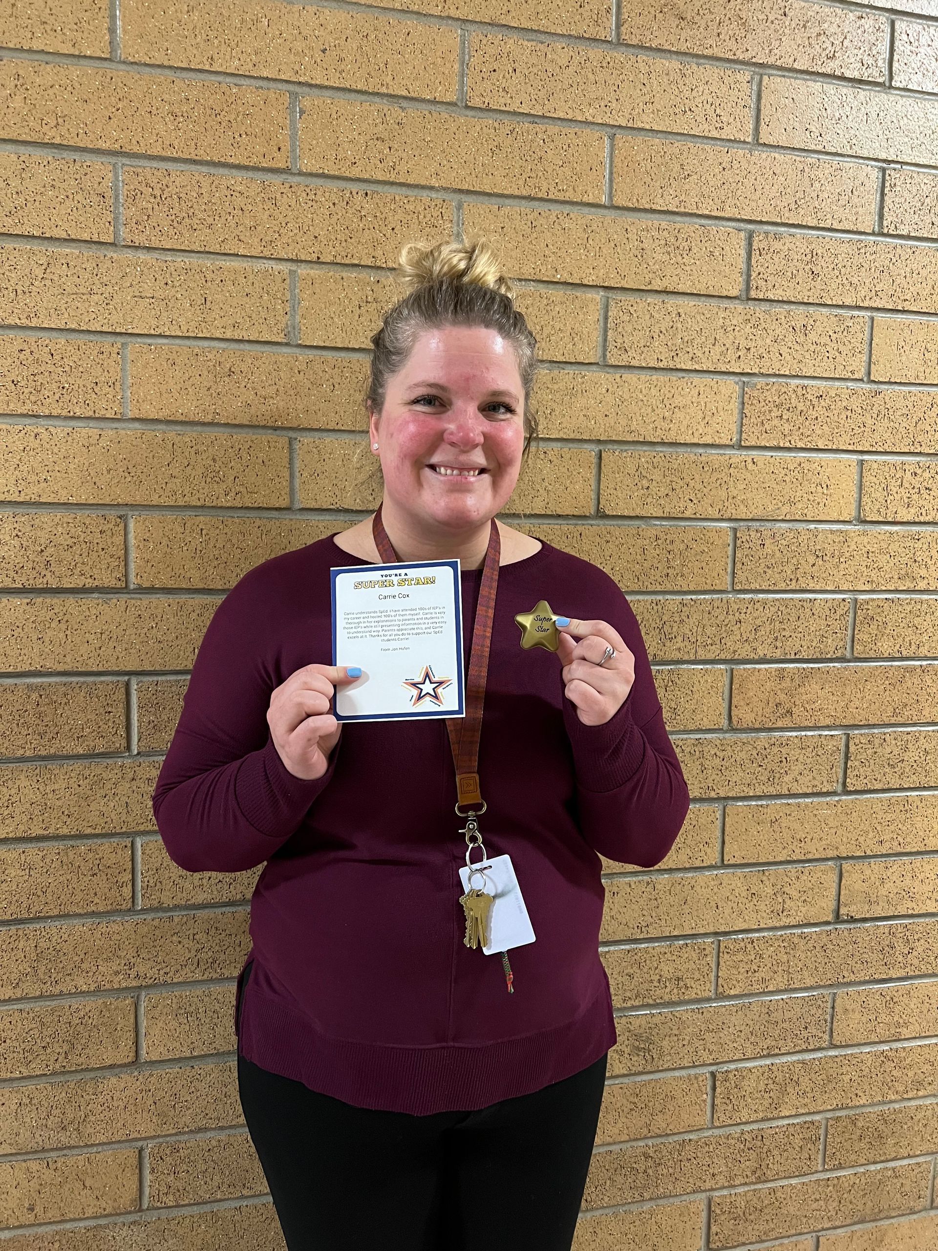 Woman in maroon sweater holding a certificate and smiling in front of a brick wall.