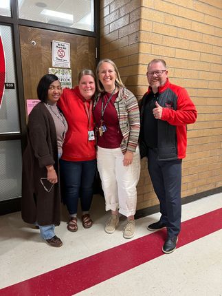Four people posing together in a hallway, smiling in front of a brick wall.