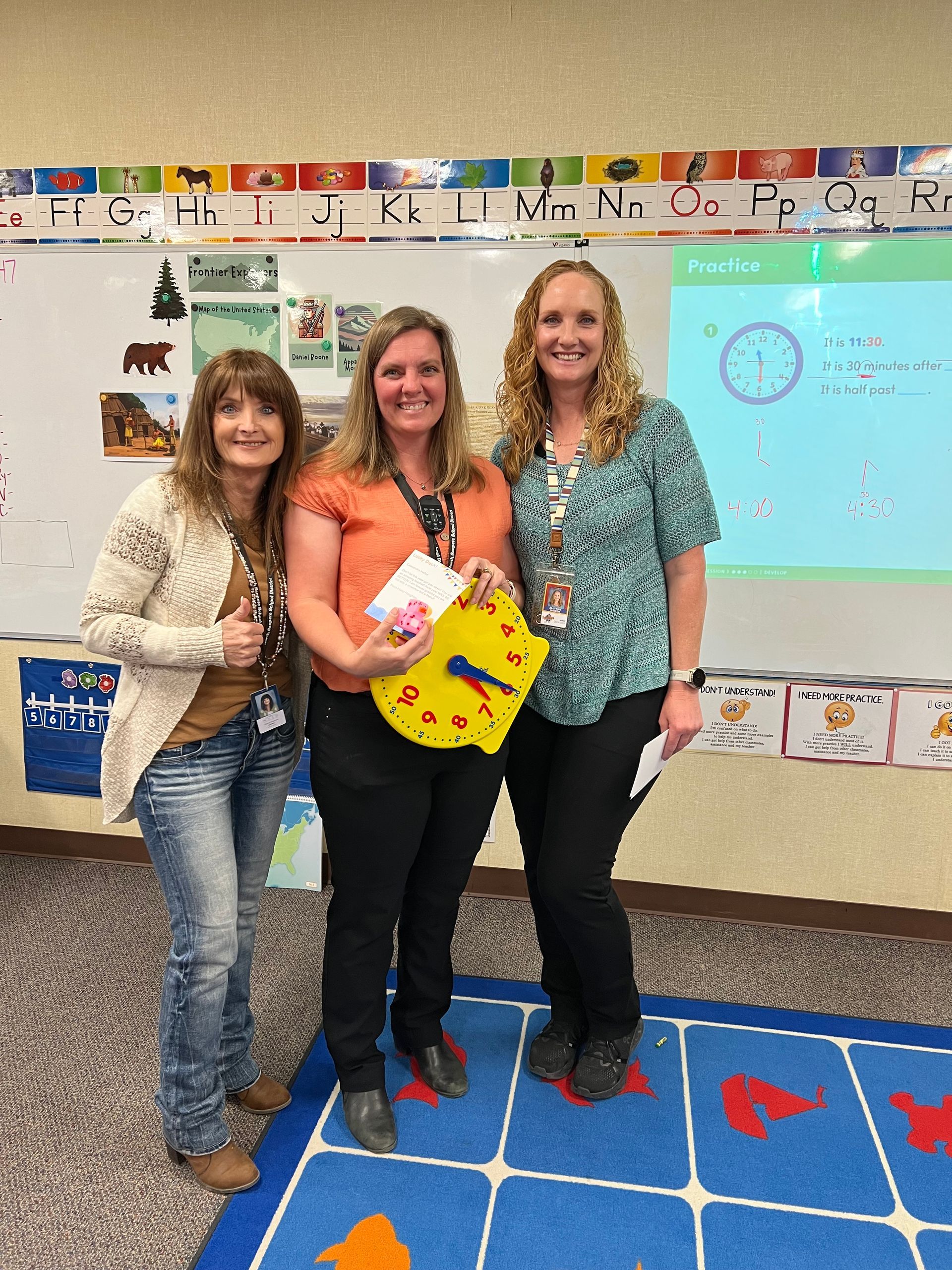 Three women are posing for a picture in front of a white board with letters on it
