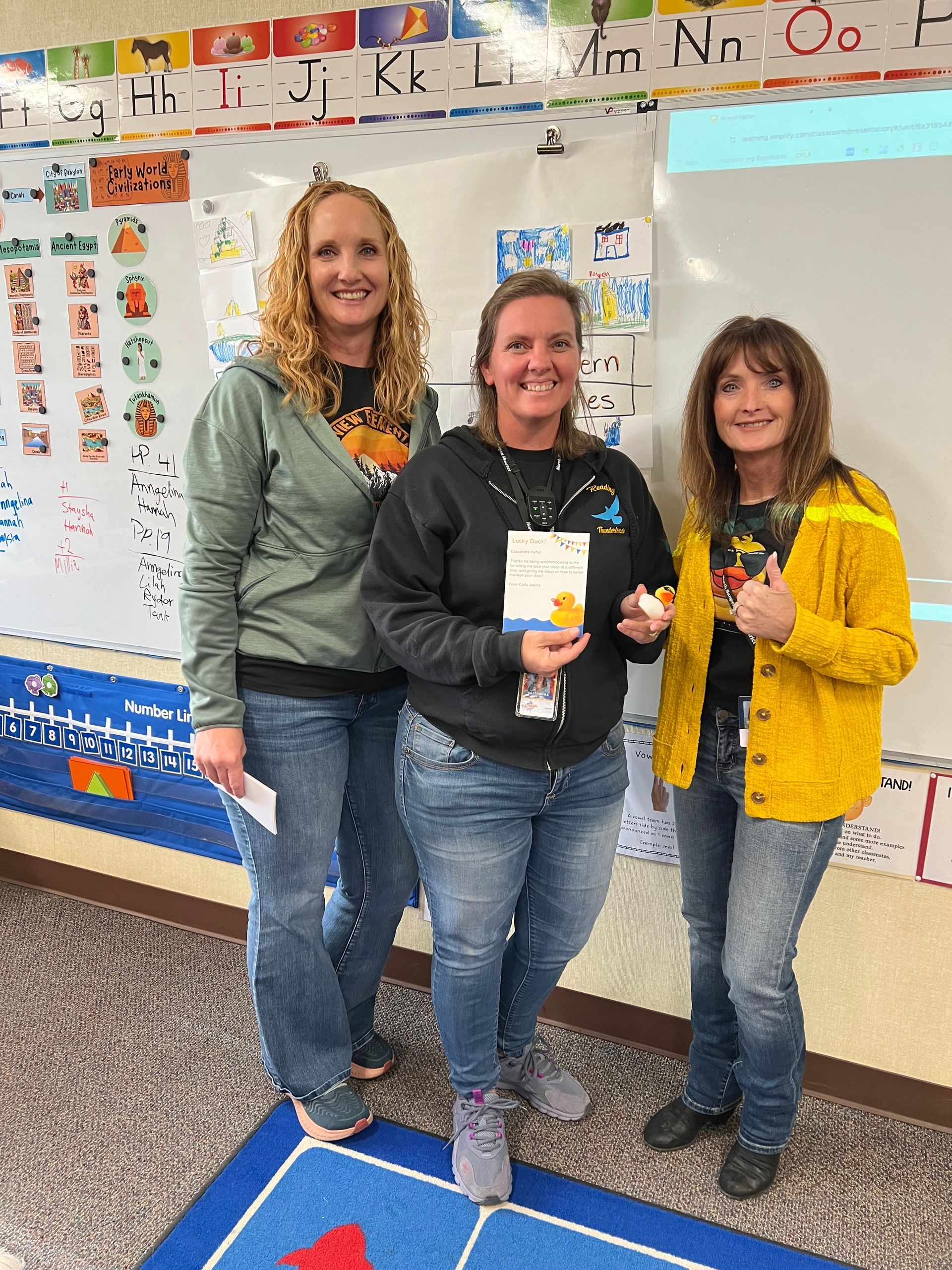 Three women are standing next to each other in a classroom.