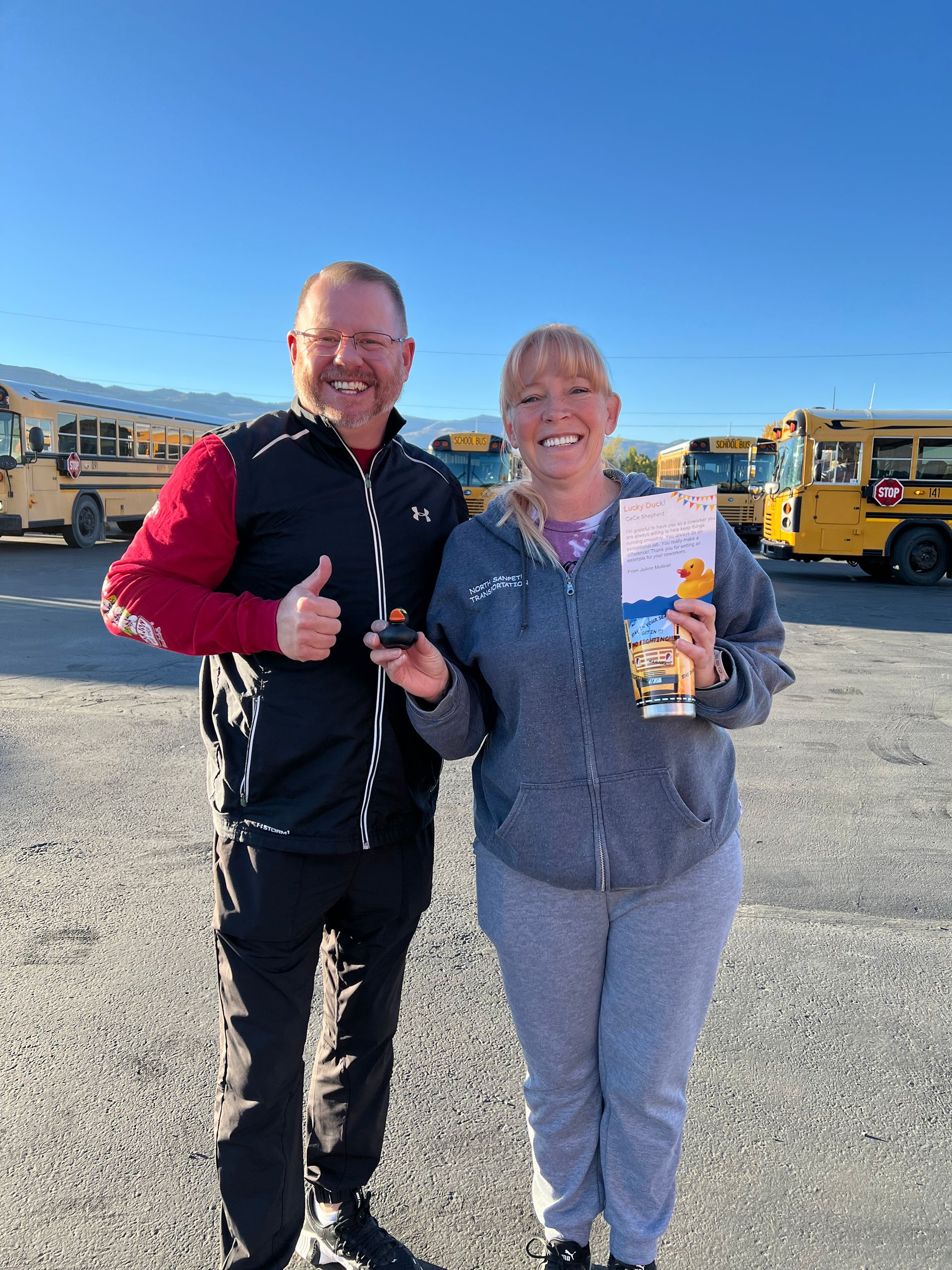 A man and a woman are standing next to each other in front of school buses.