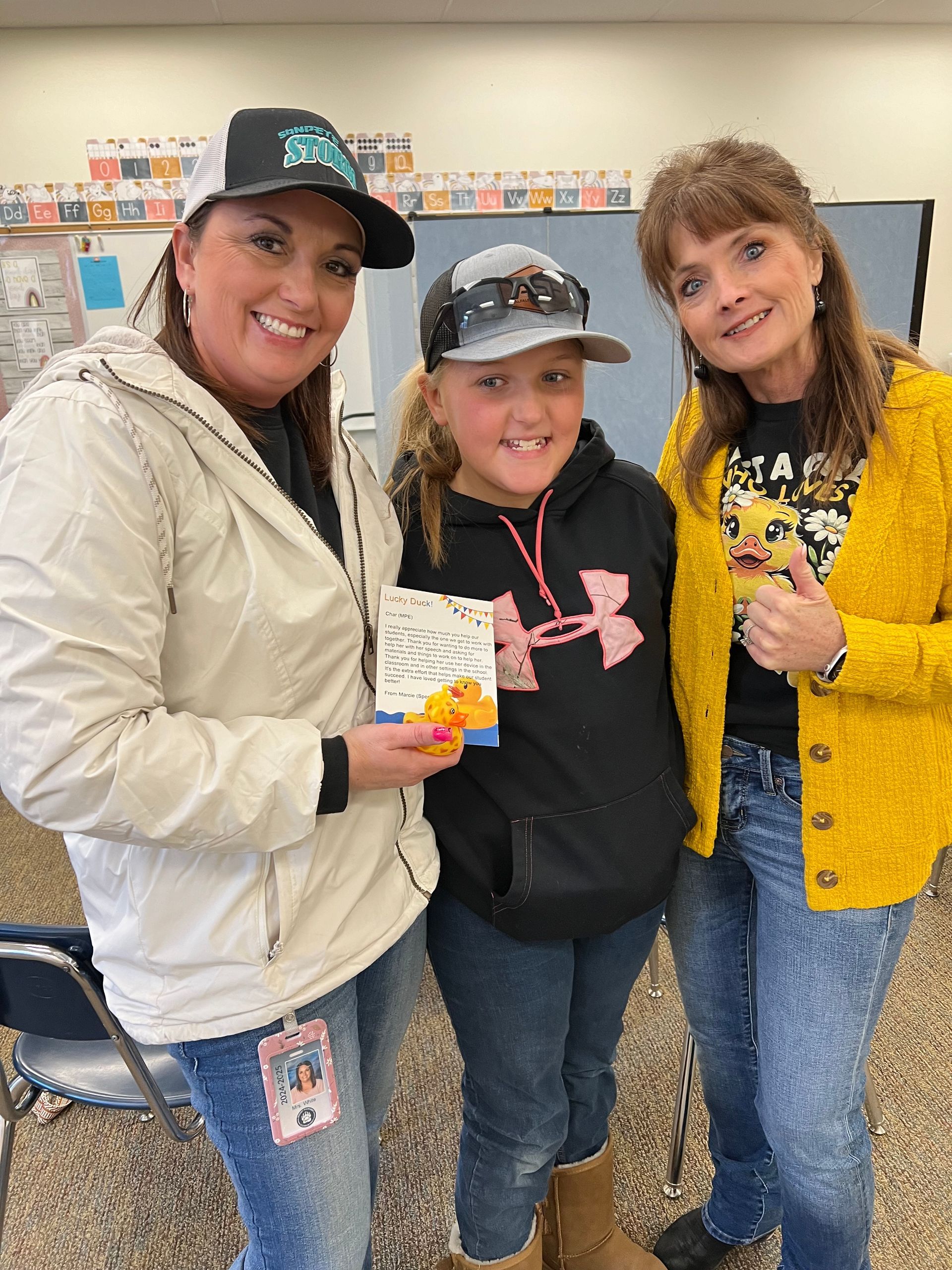 Three women are standing next to each other in a classroom.