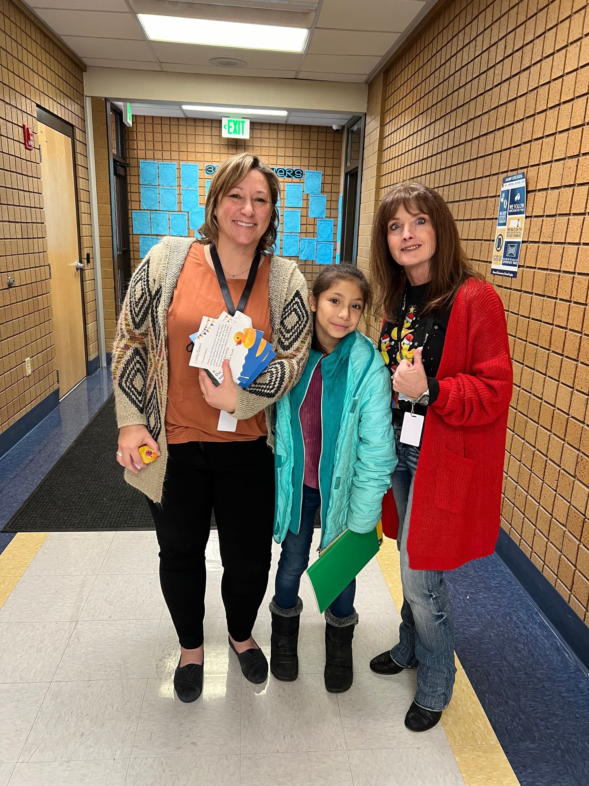 Three women are standing next to each other in a hallway.