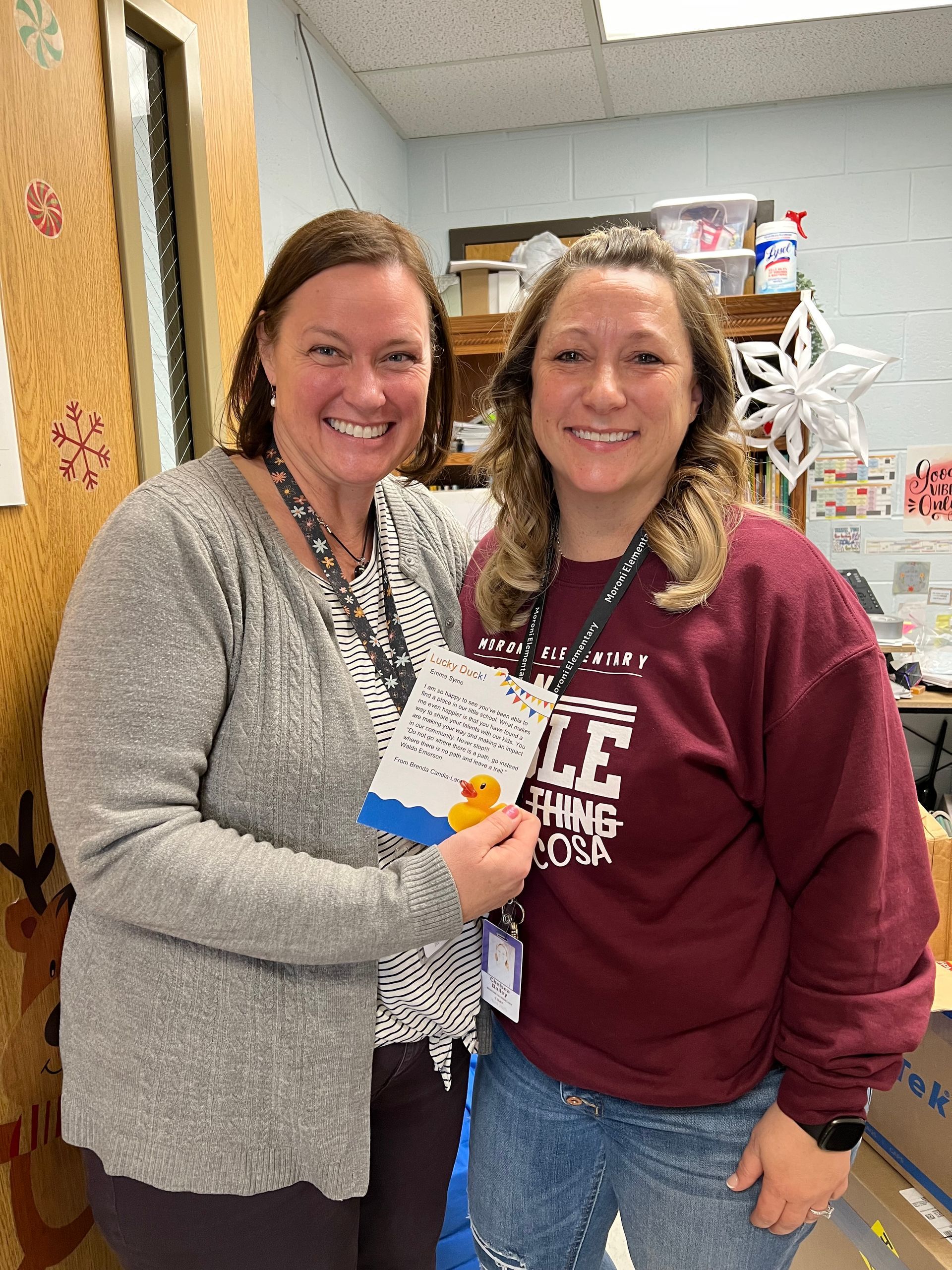 Two women are standing next to each other in a room and one of them is holding a card.