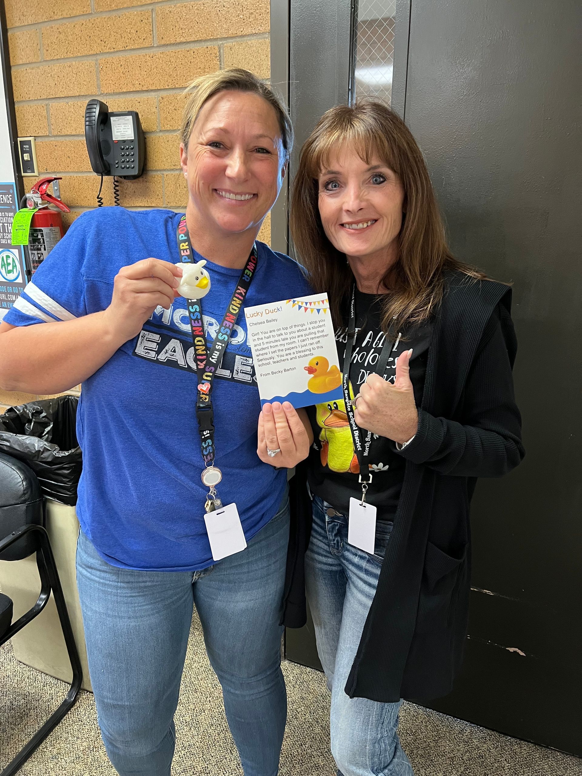 Two women are standing next to each other holding a card and a rubber duck.