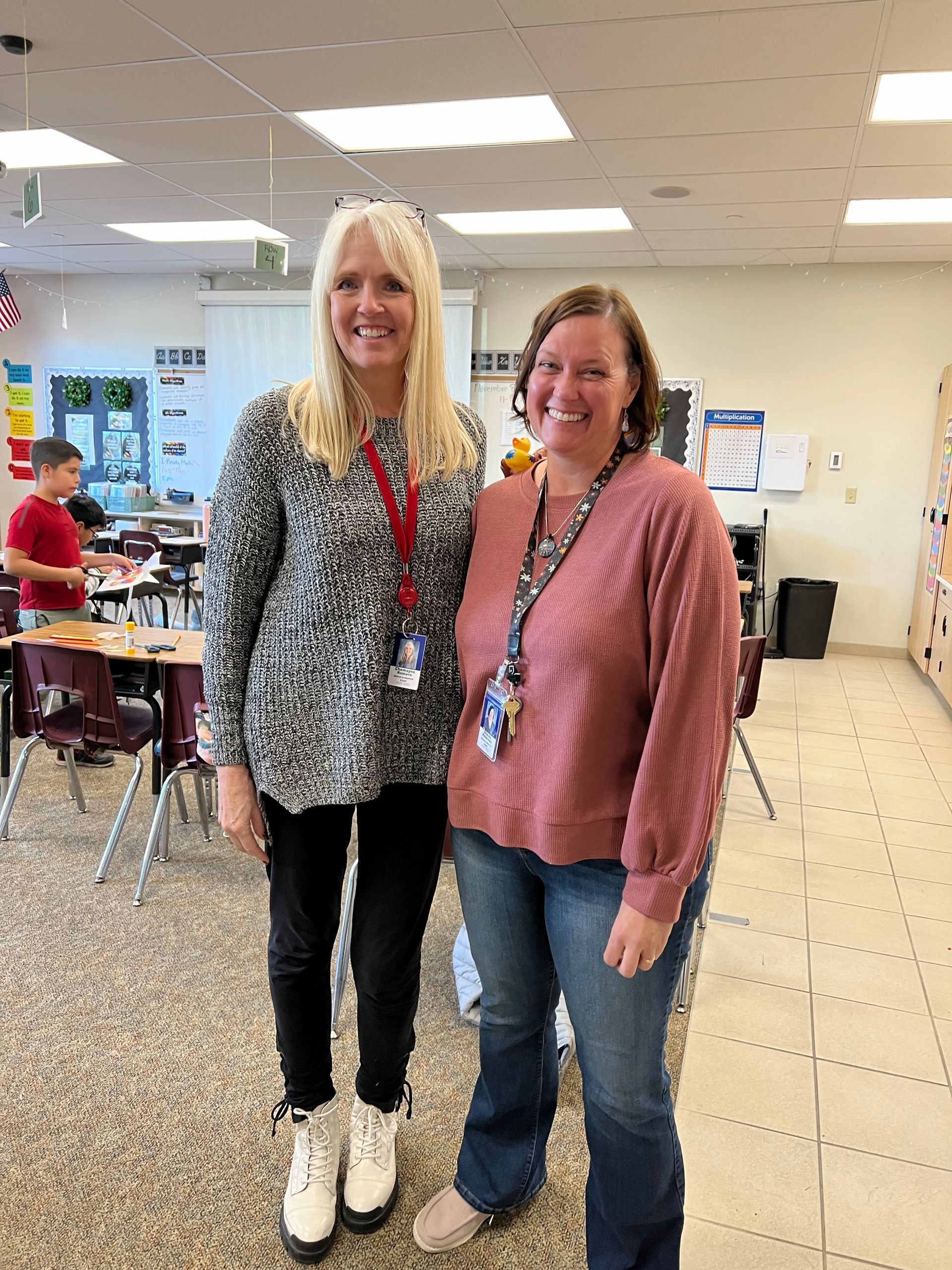 Two women are posing for a picture in a classroom.