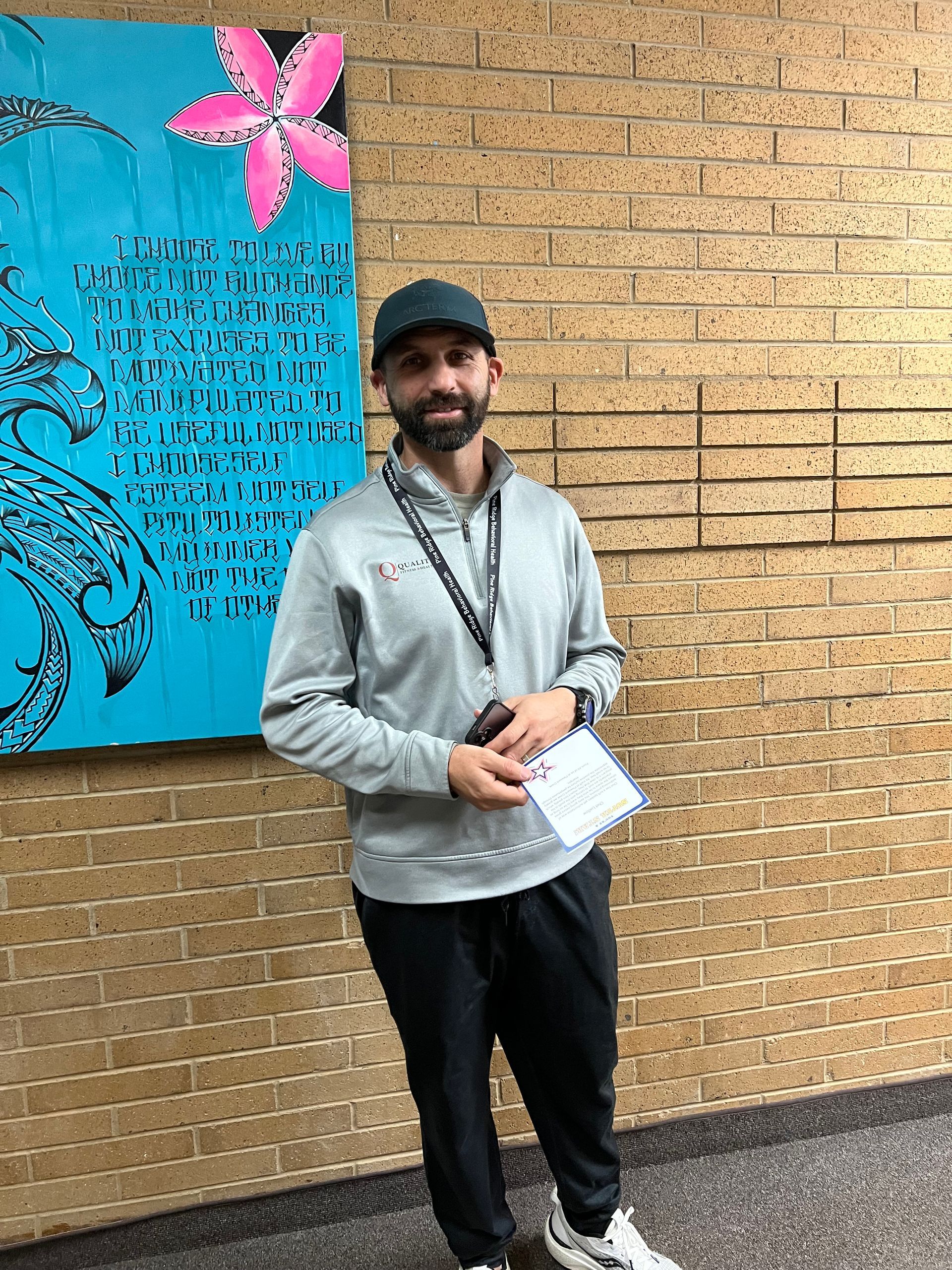Man wearing a gray sweatshirt and cap, standing in a hallway near a teal poster.