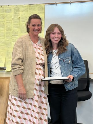 Two people stand smiling in an office, holding a document in front of yellow sticky notes.