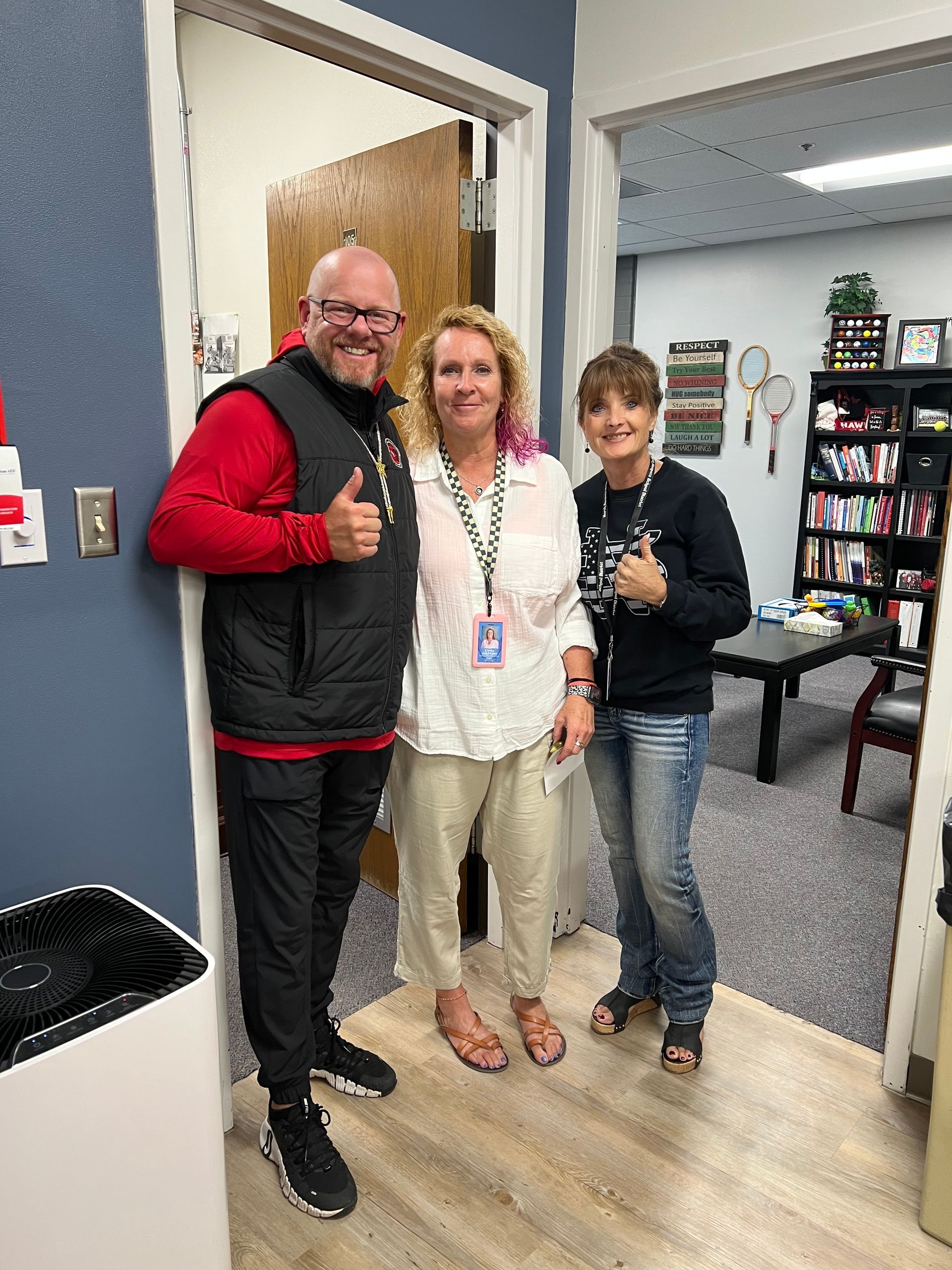 Three people smiling and giving thumbs up in an office setting.
