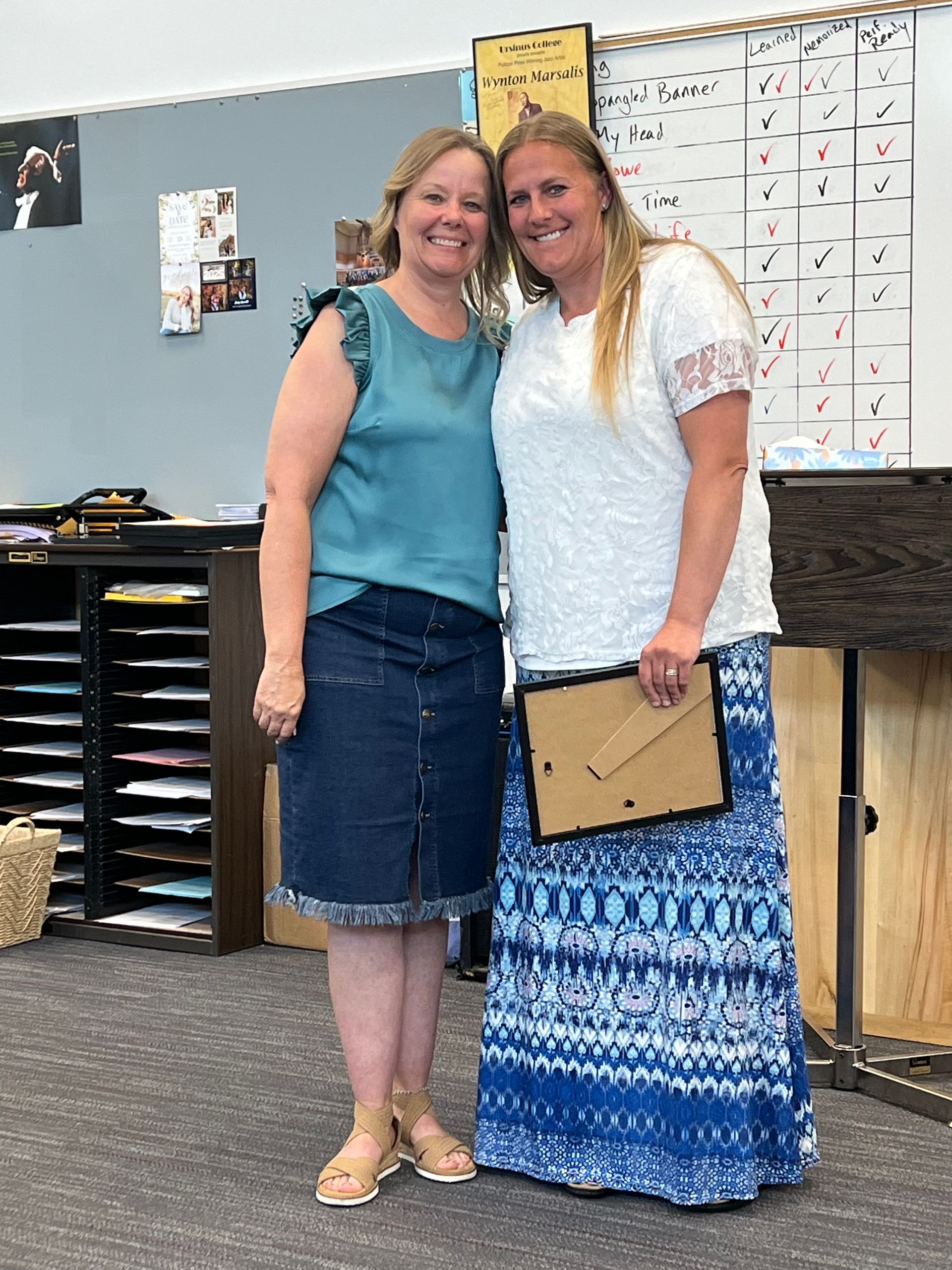 Two women are standing next to each other in a classroom holding a picture frame.