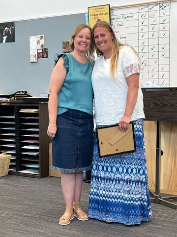 Two women are standing next to each other in a classroom holding a picture frame.