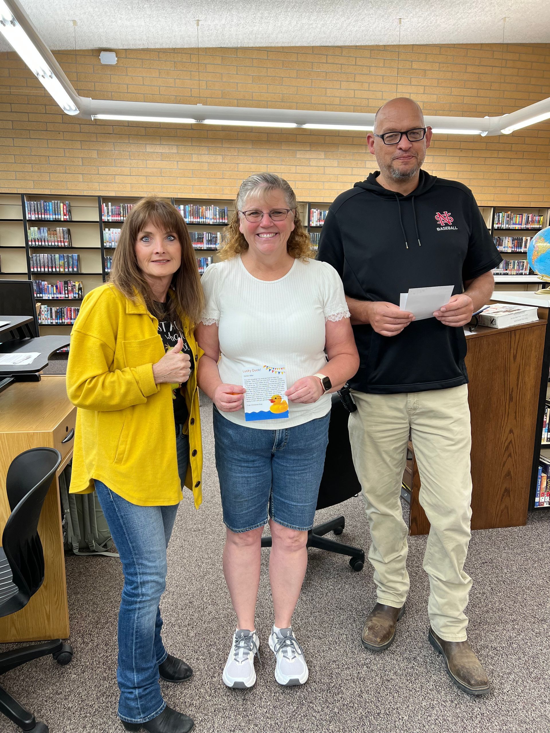 Three people are standing next to each other in a library.