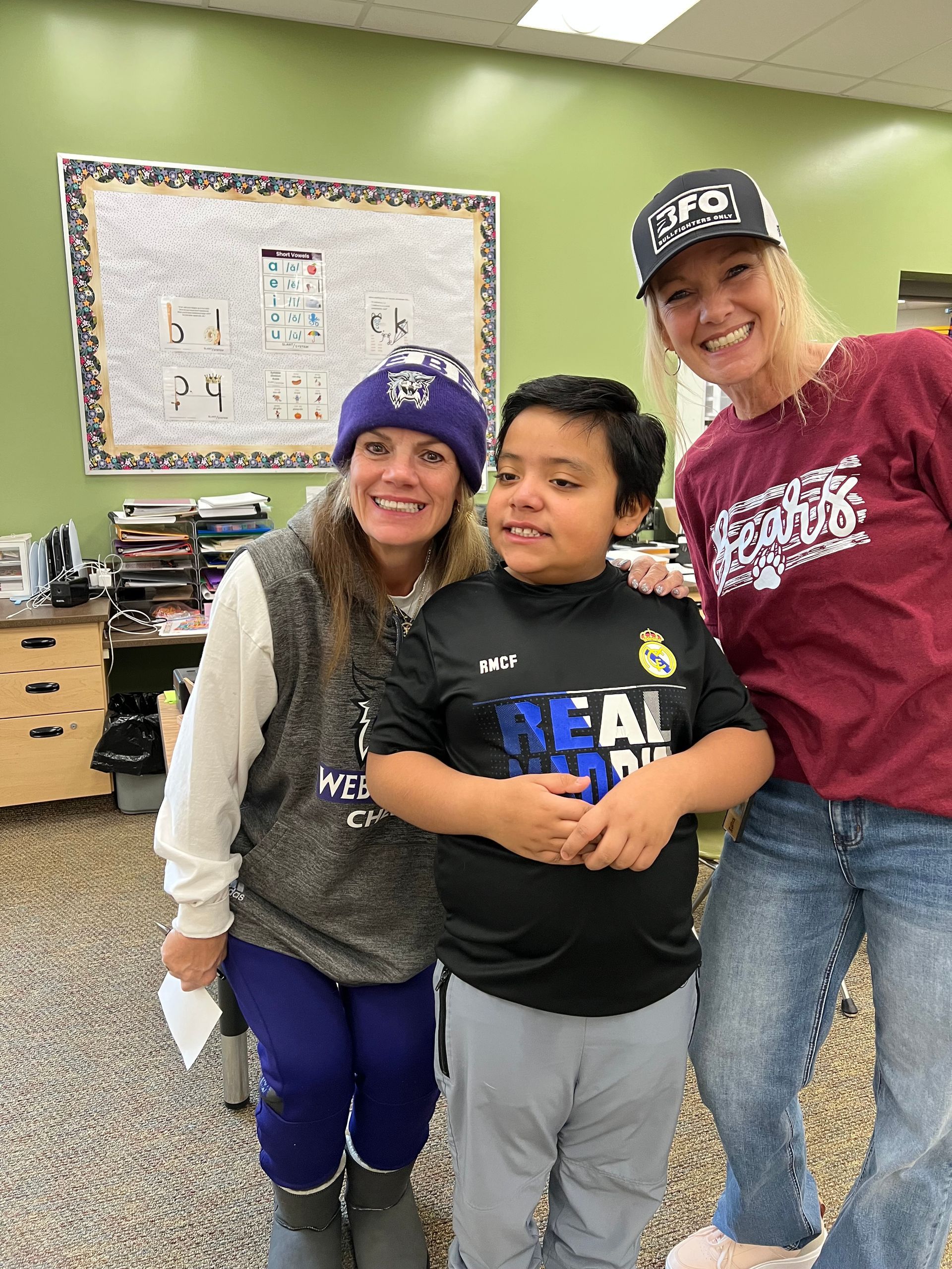 Two women wearing baseball caps with a male student smiling.
