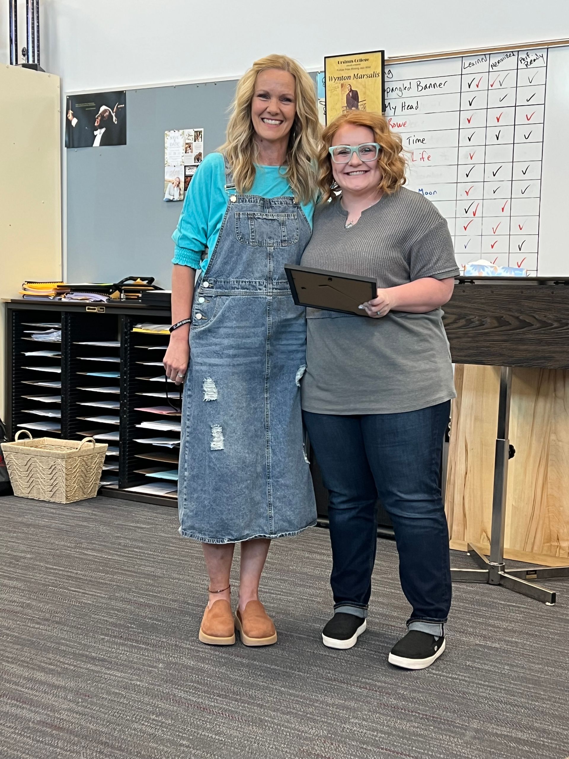 Two women are standing next to each other in a classroom holding a tablet.