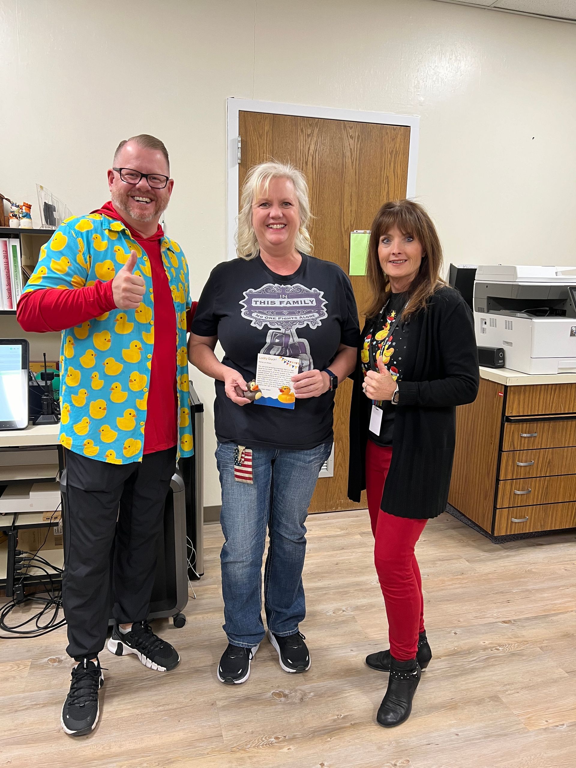 A man and two women are standing next to each other in an office giving a thumbs up.