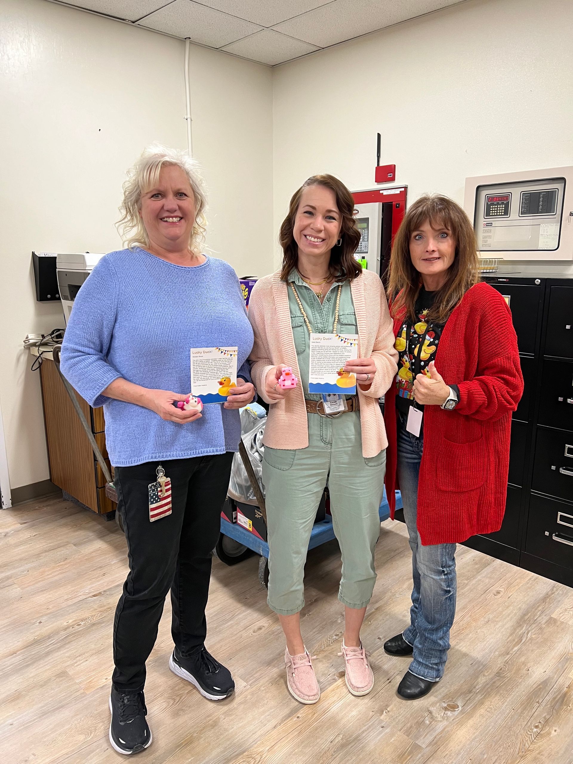 Three women are standing next to each other in a room holding cards.