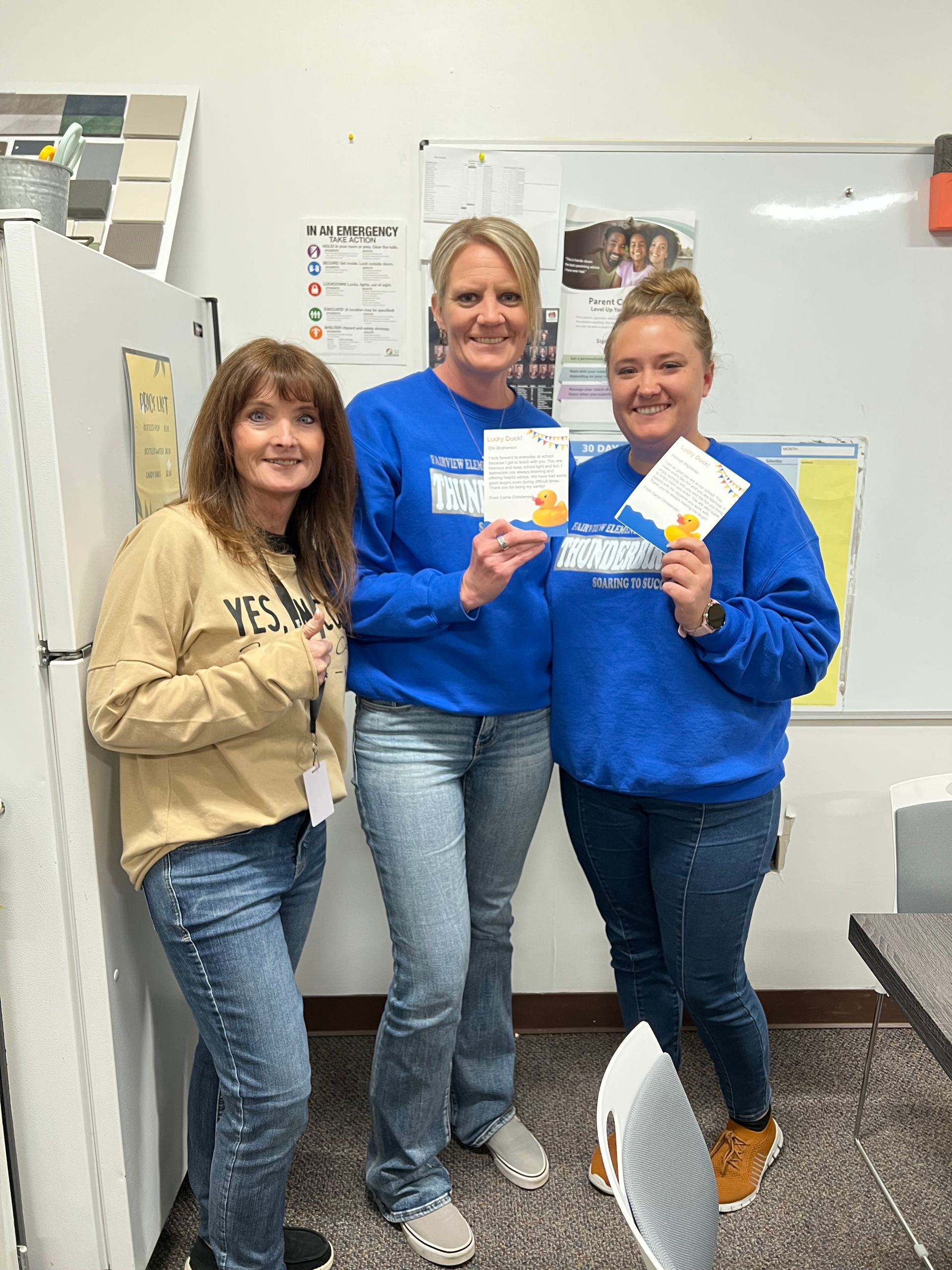Three women are standing next to each other in a classroom.