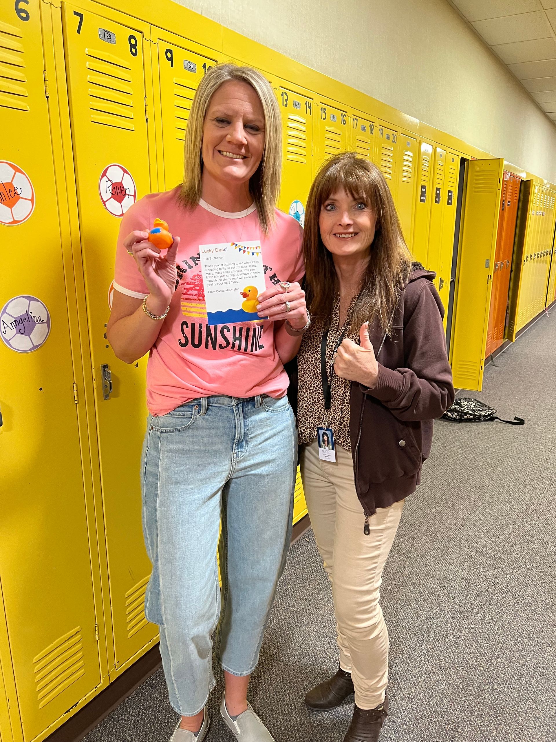 Two women are standing next to each other in front of yellow lockers.