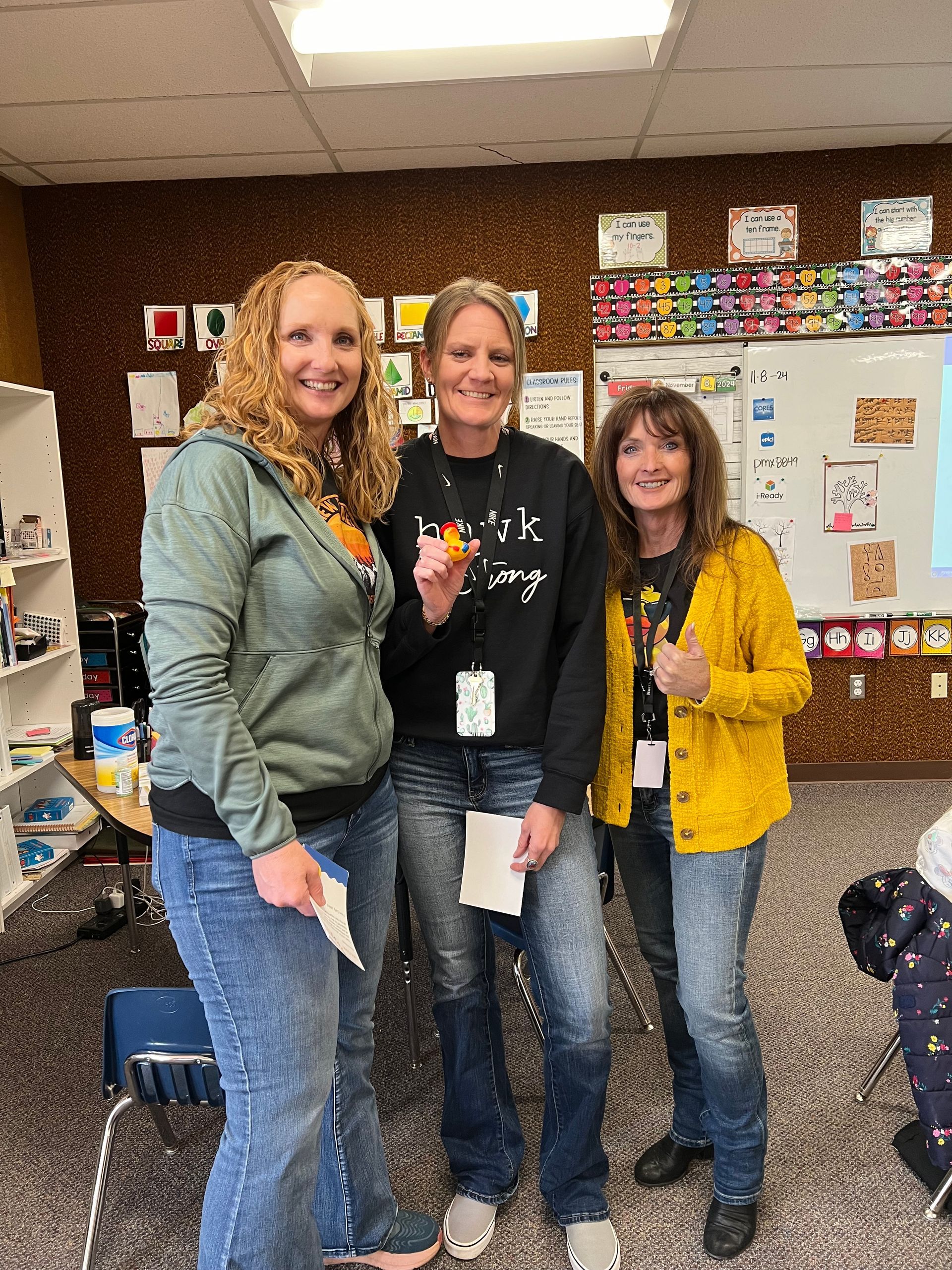 Three women are posing for a picture in a classroom.