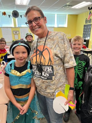 A teacher and two students in Halloween costumes in a classroom.