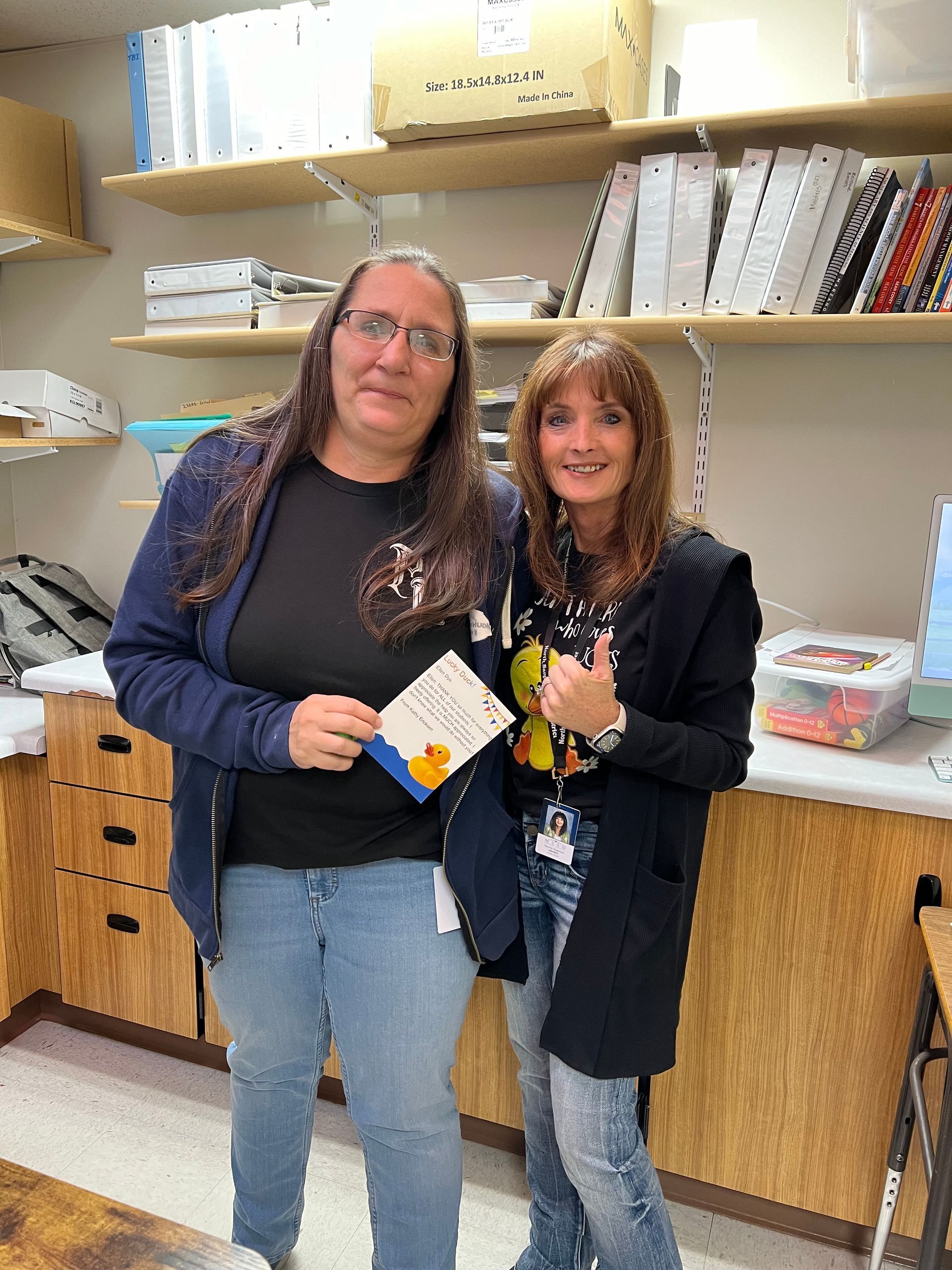 Two women are standing next to each other in a room holding a card.