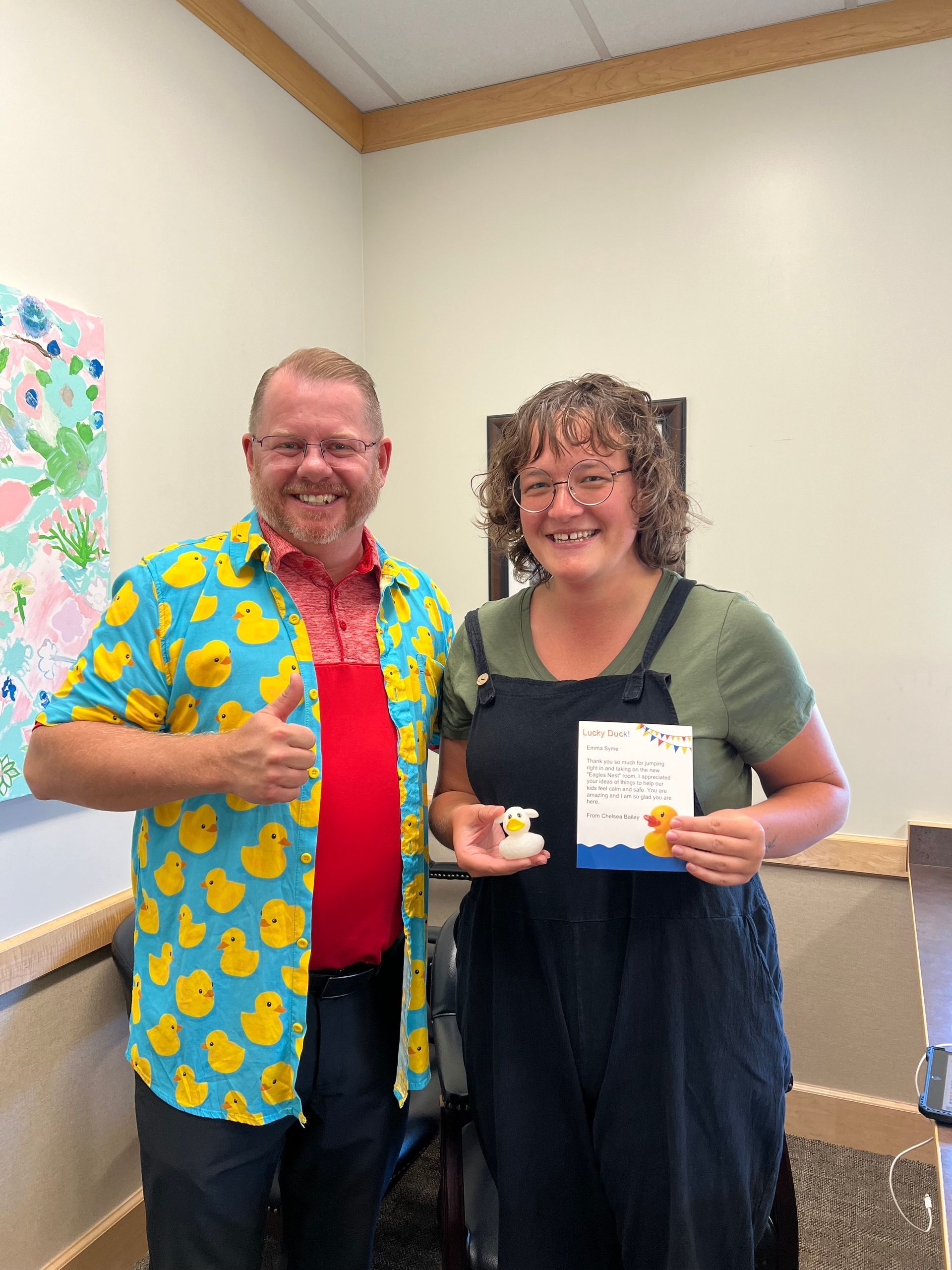 A man in a duck shirt is standing next to a woman holding a rubber duck.