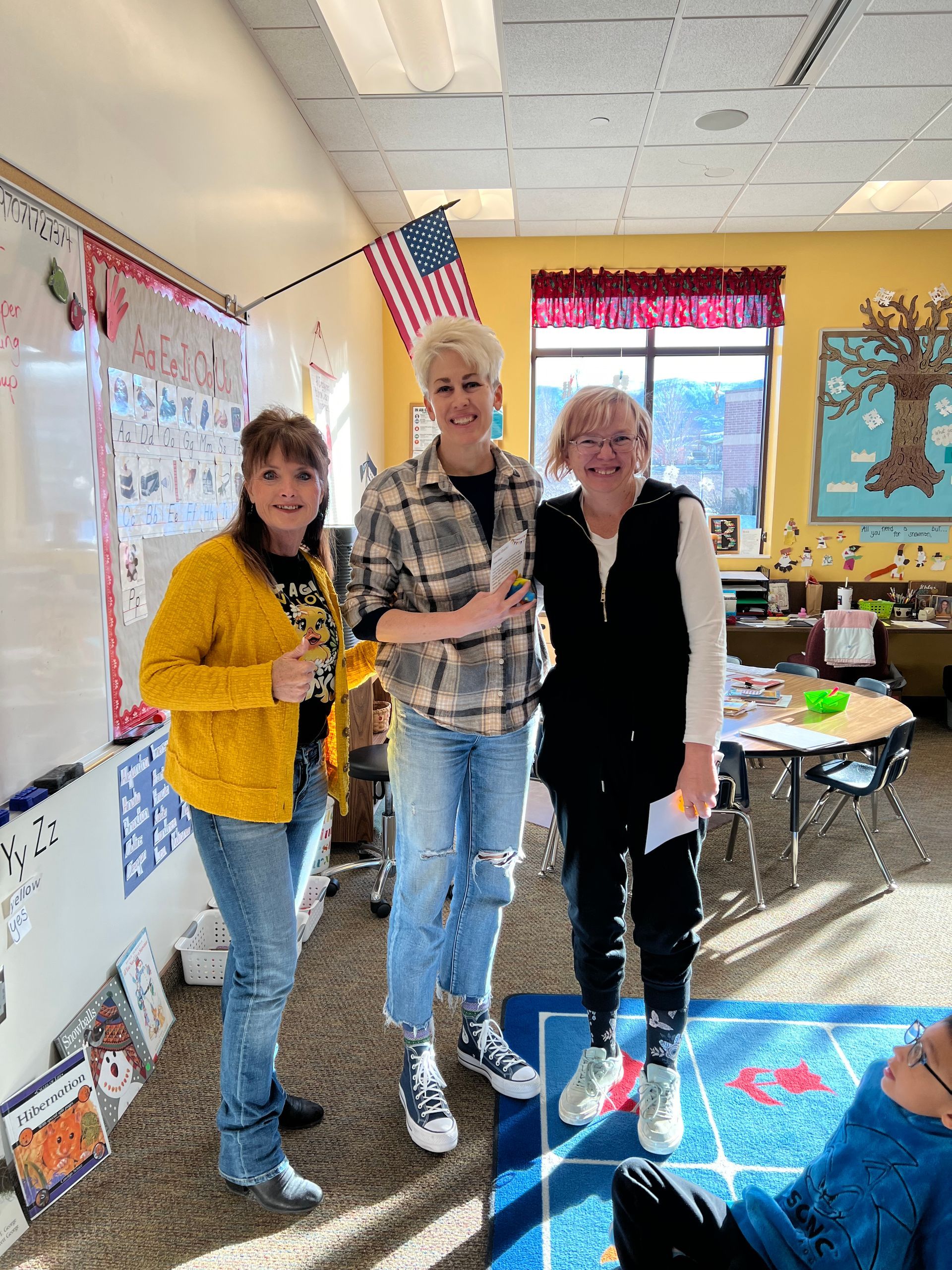 Three women are posing for a picture in a classroom.