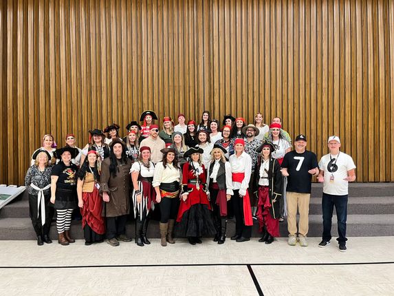 Group of people in pirate costumes posing for a photo against a wood-paneled wall.