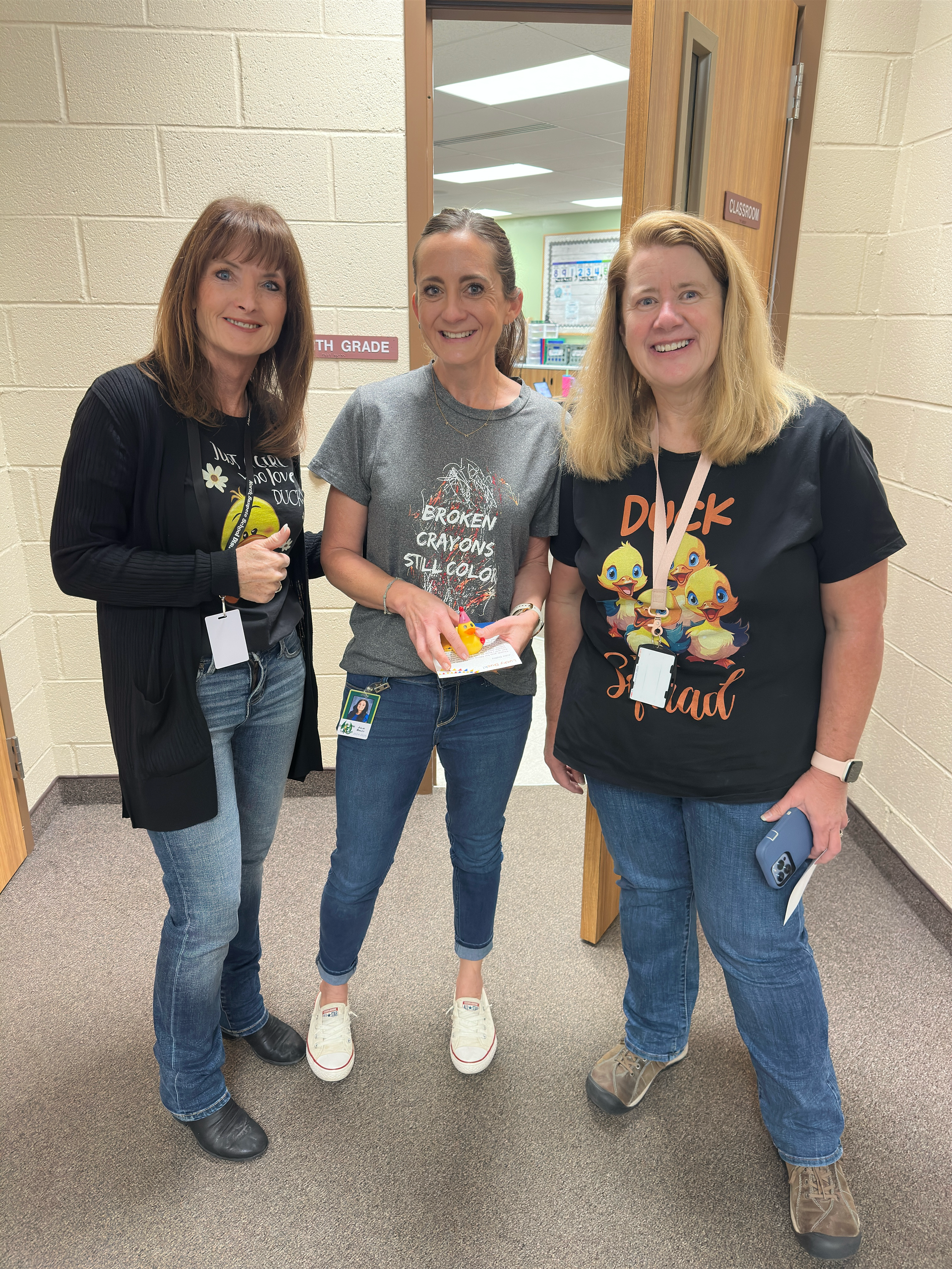 Three women are standing next to each other in a hallway.