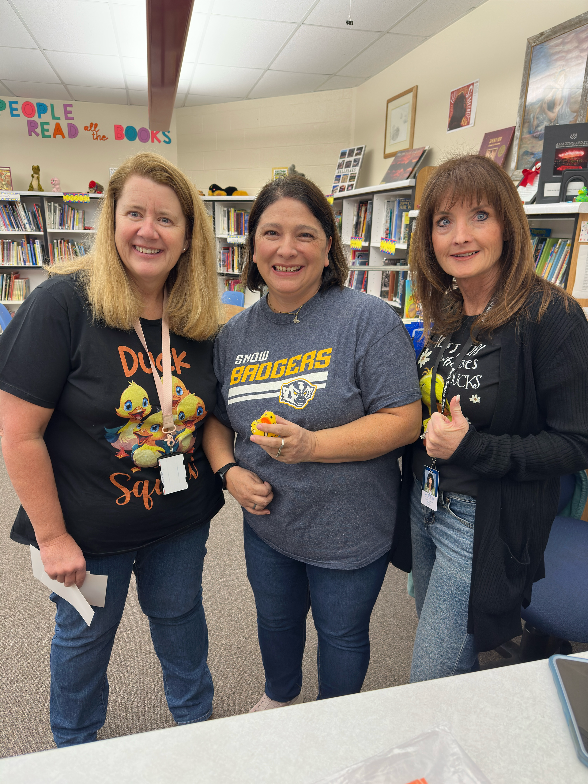 Three women are standing next to each other in a library.