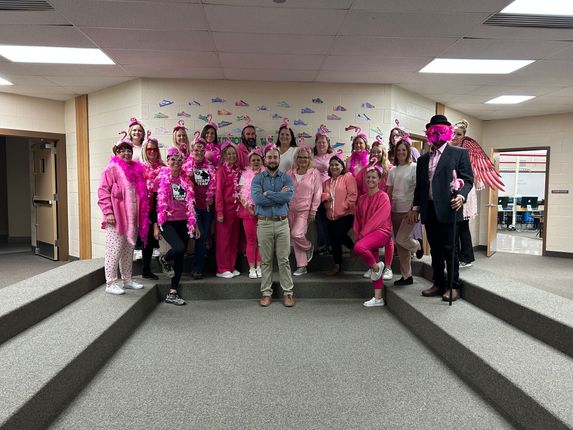 Group of people in pink attire, posing on steps in a hallway.