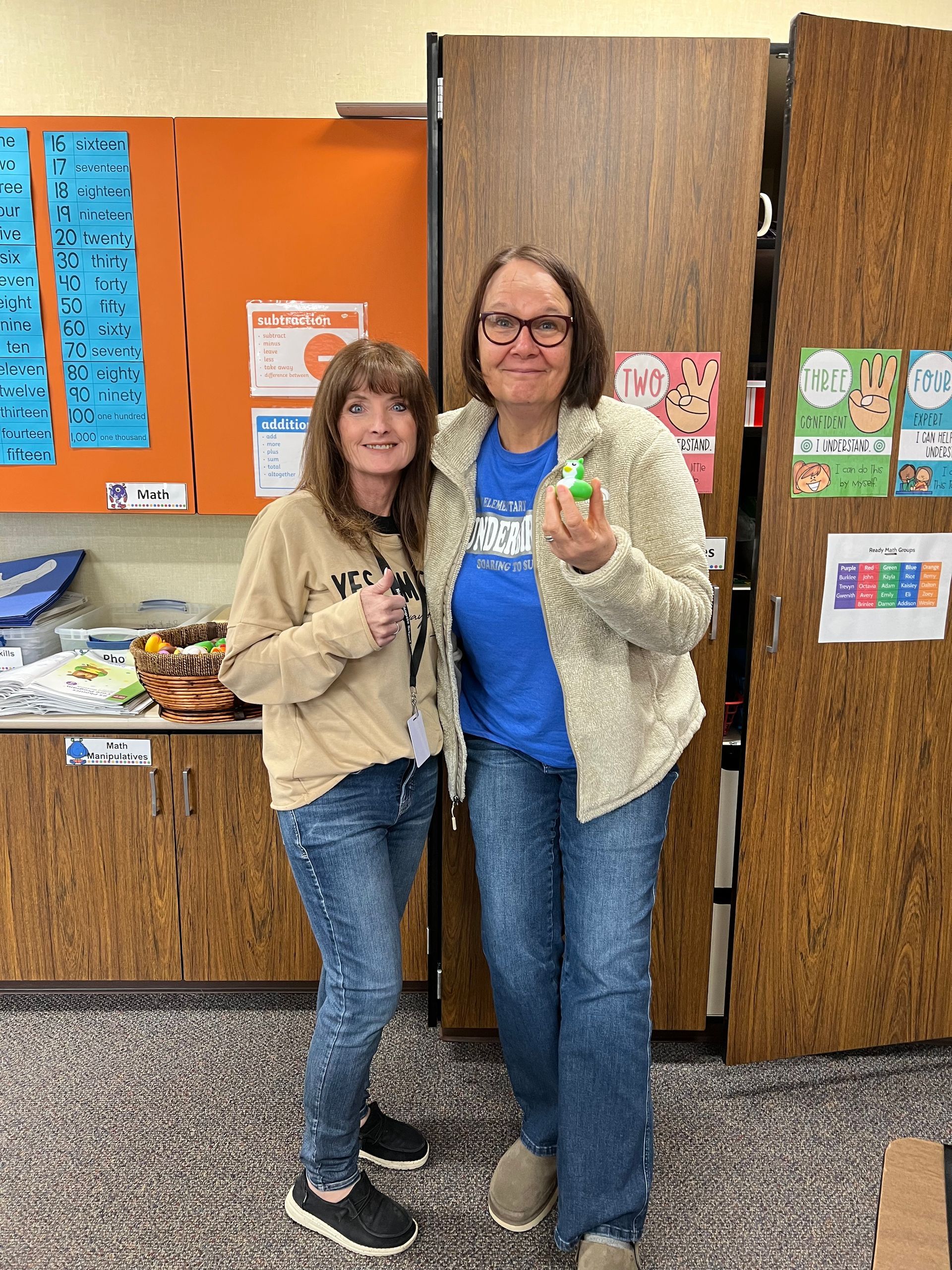 Two women are standing next to each other in a classroom holding a green object.
