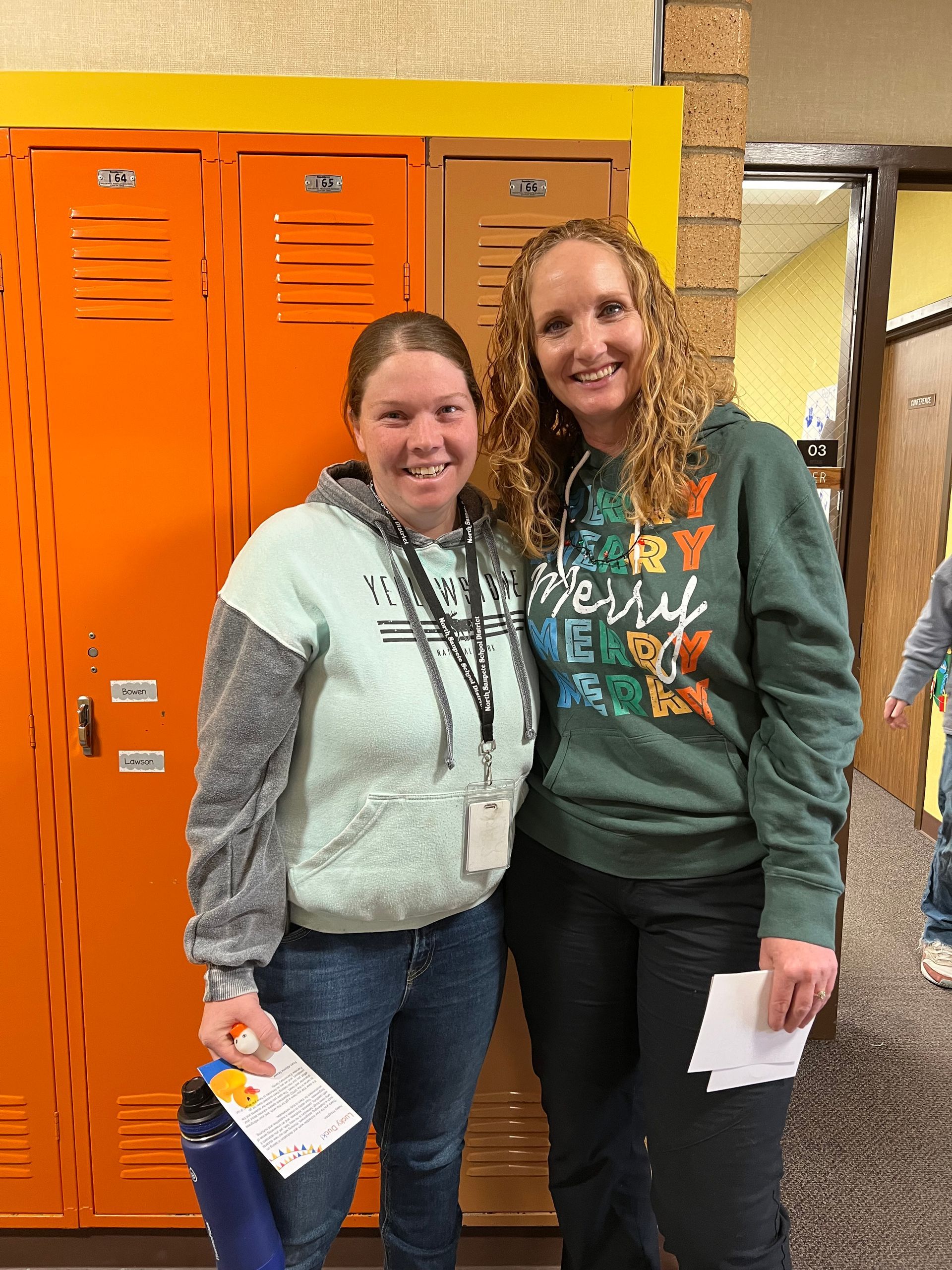 Two women are posing for a picture in front of orange lockers.