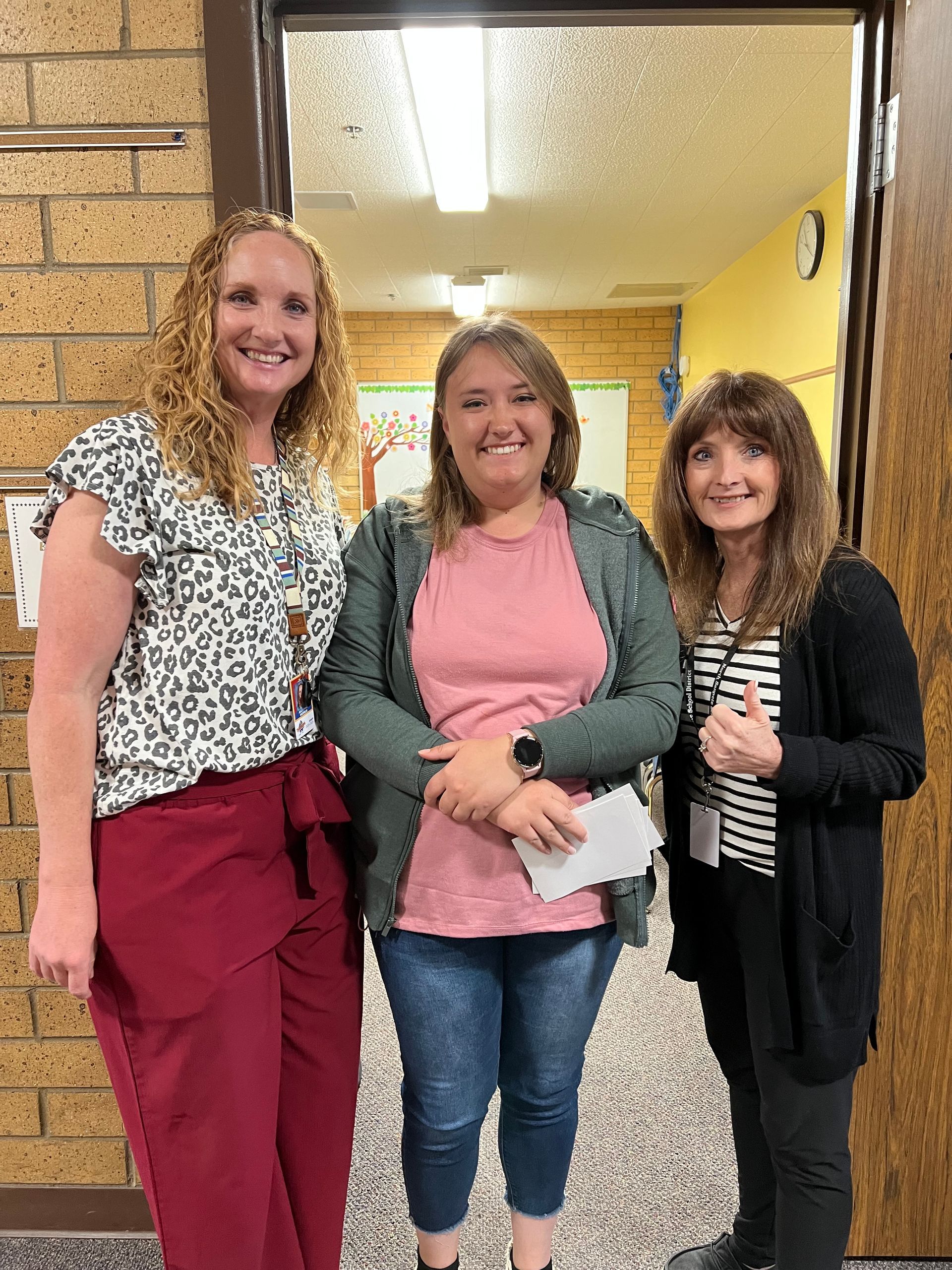 Three women are standing next to each other in a hallway.