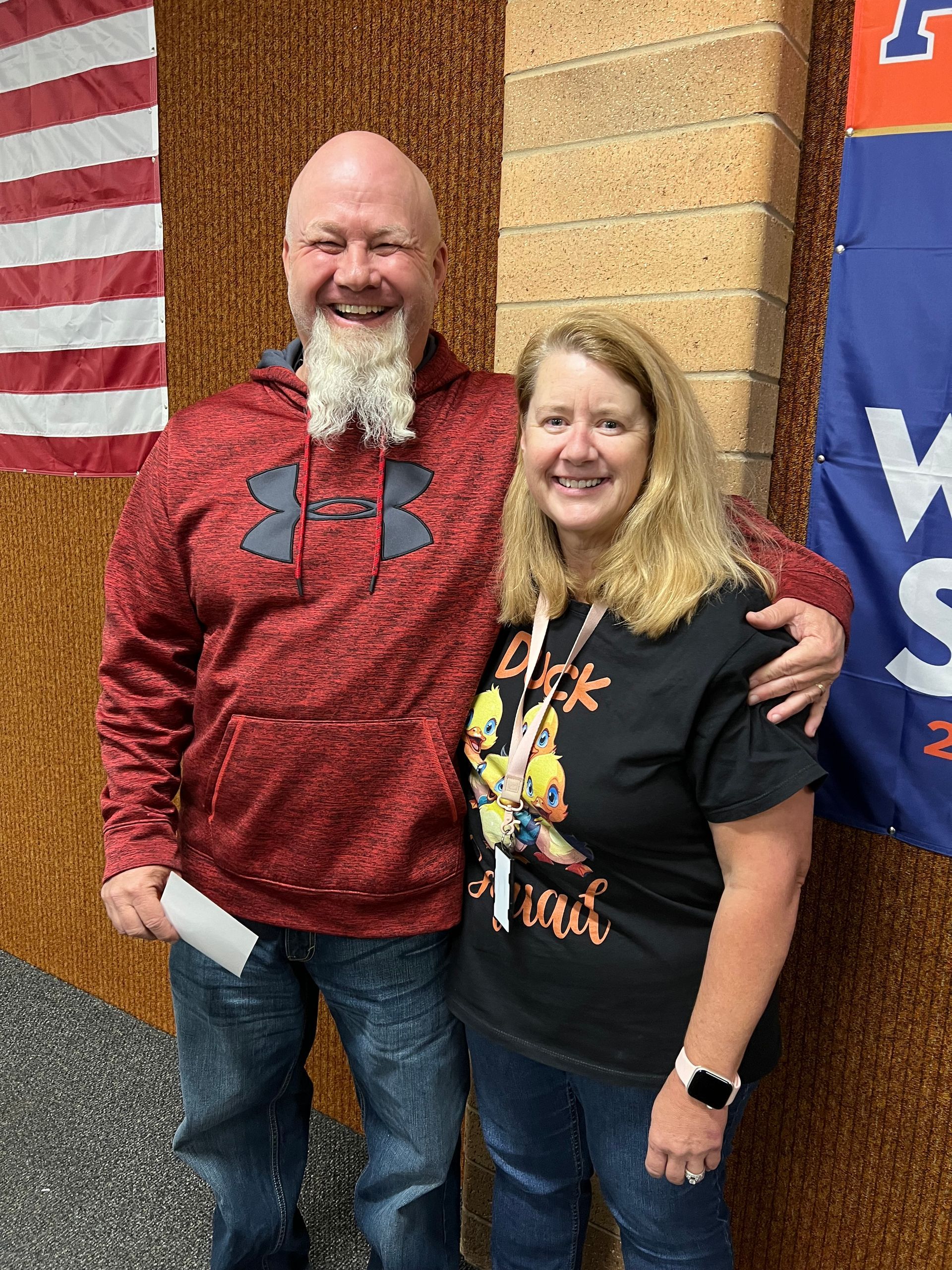 A man and a woman are posing for a picture in front of an american flag.