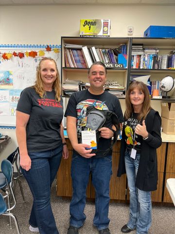 A man and two women are standing next to each other in a classroom.