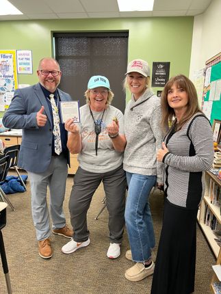 Four people smiling, one man with a thumbs up, in a classroom.