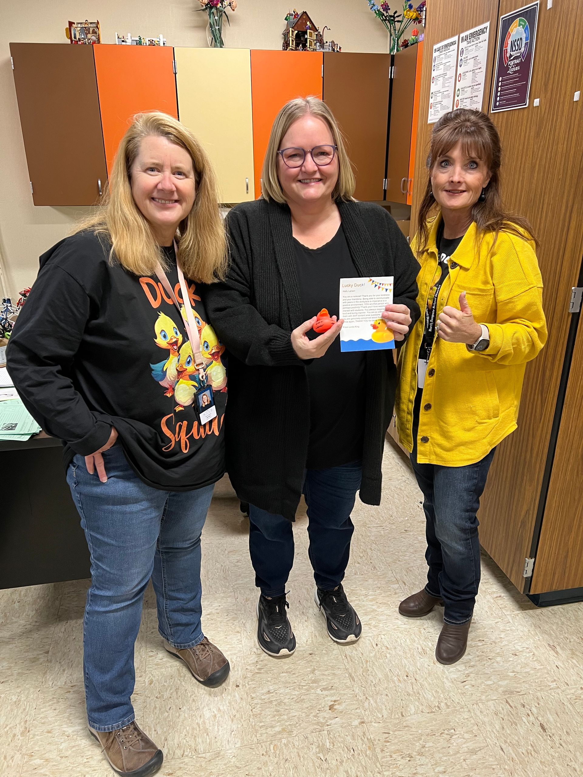 Three women are standing next to each other in a room holding a book.