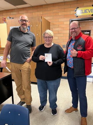 Three people posing indoors, smiling and holding a small award plaque.